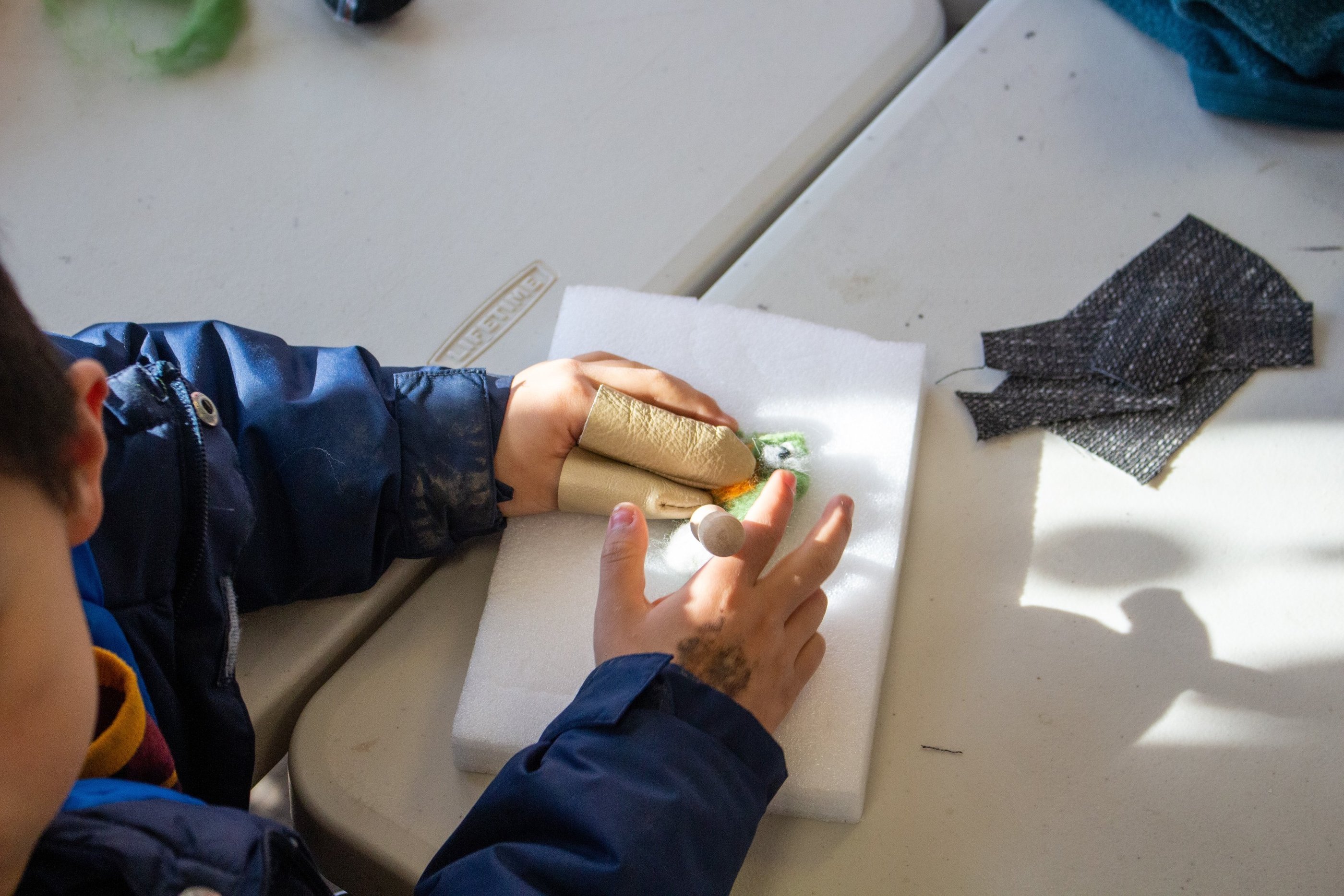 Young child's hands with finger coverings, poking pieces of wool to create a felted creature.
