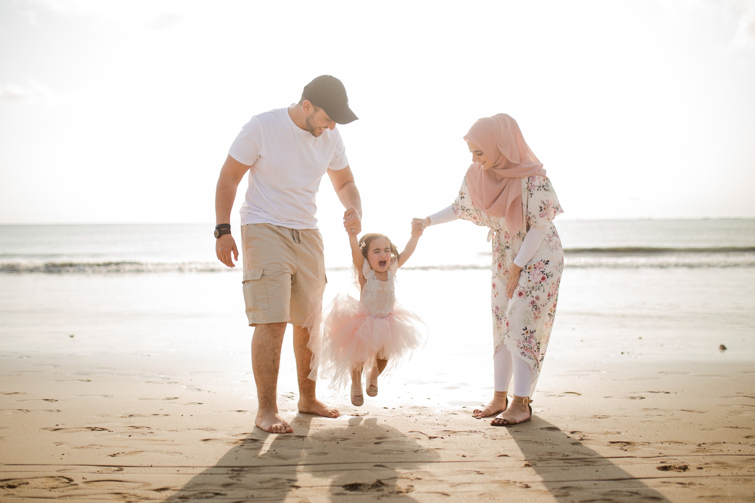 family photography Jimbaran Beach Bali parents holding hands with child on beach
