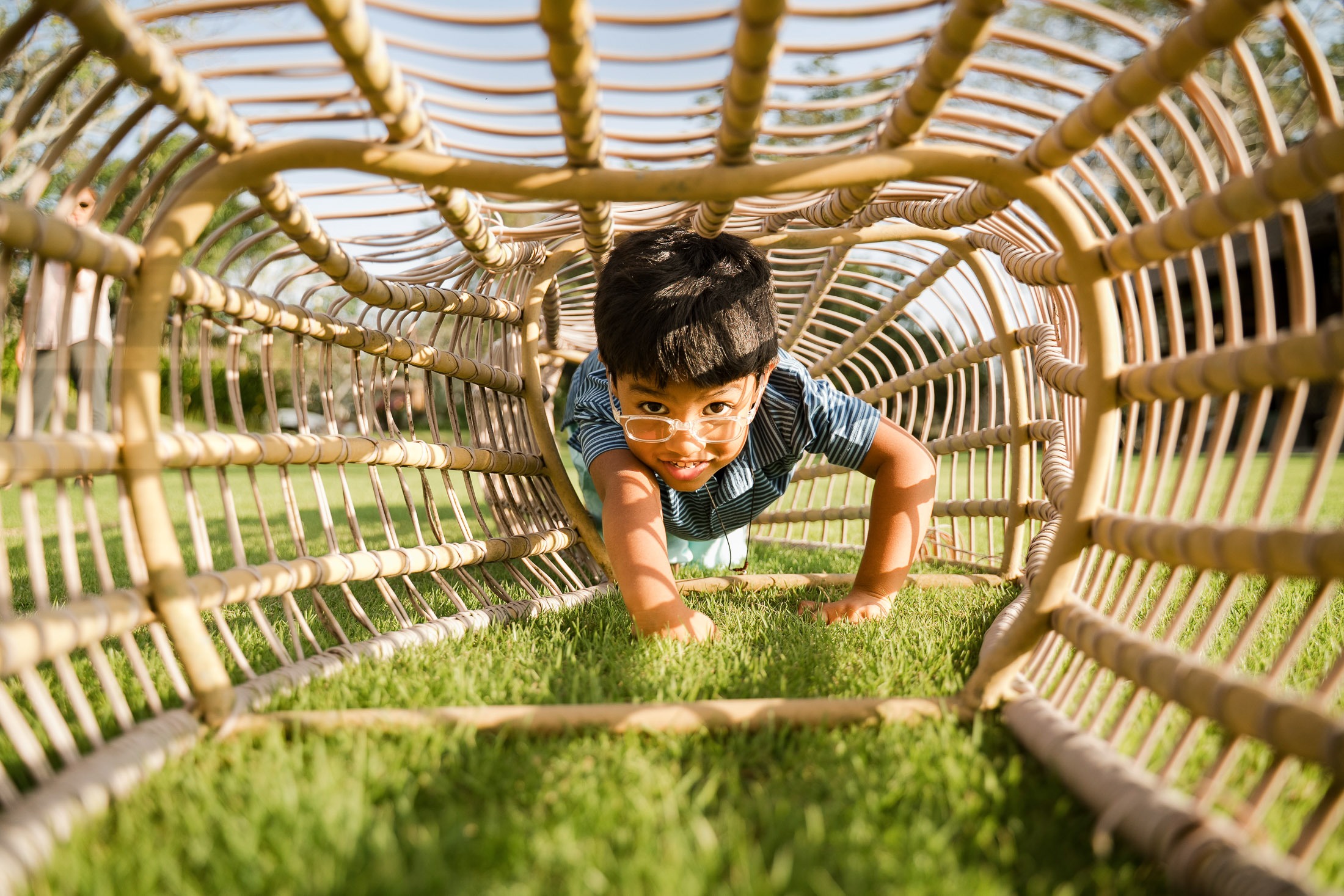 child crawling through rattan tunnel chair on the lawn at rimba by ayana bali during family photography