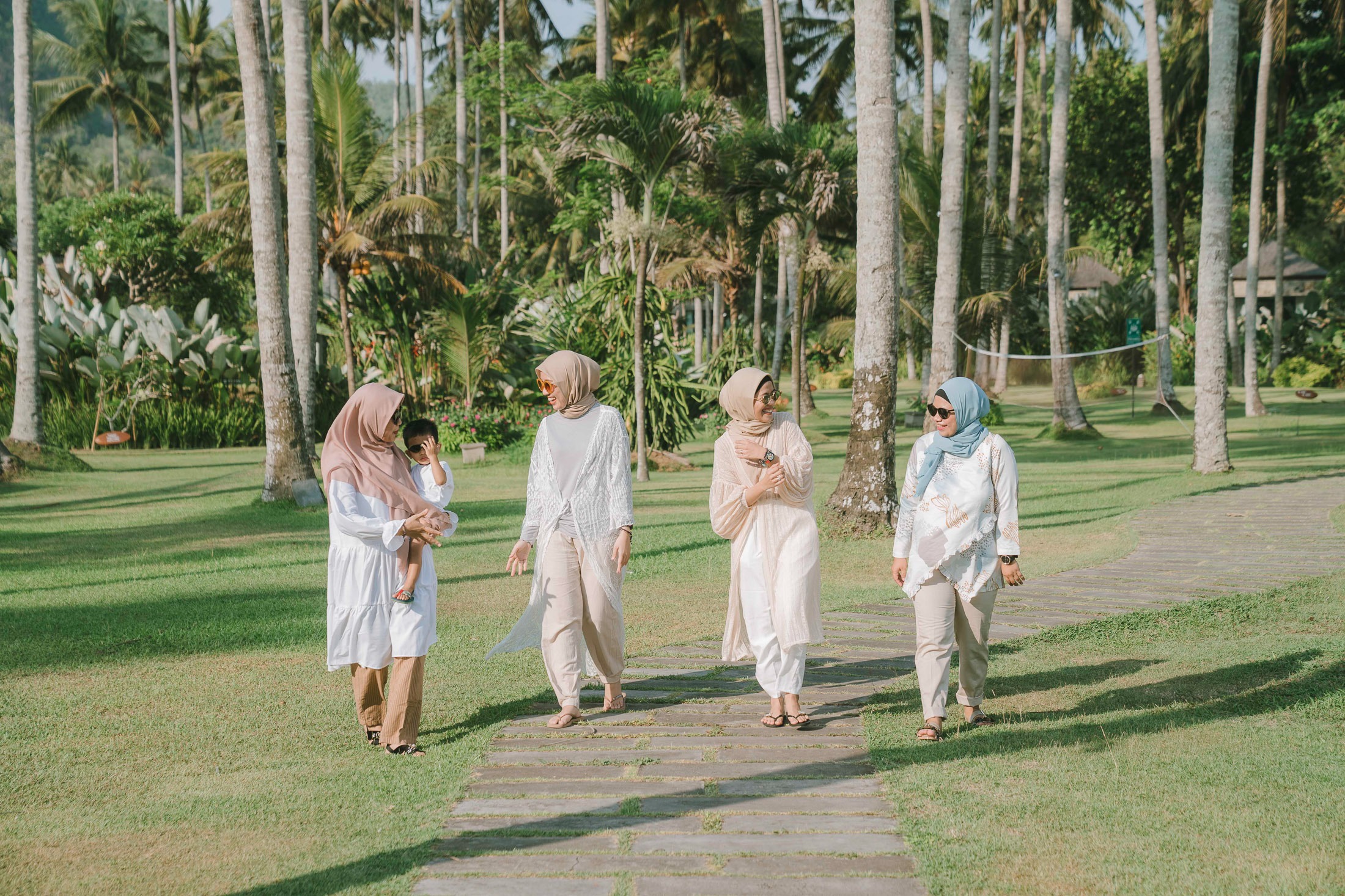 Friends walking together across palm garden lawn during photoshoot at Candi Beach Resort Karangasem Bali