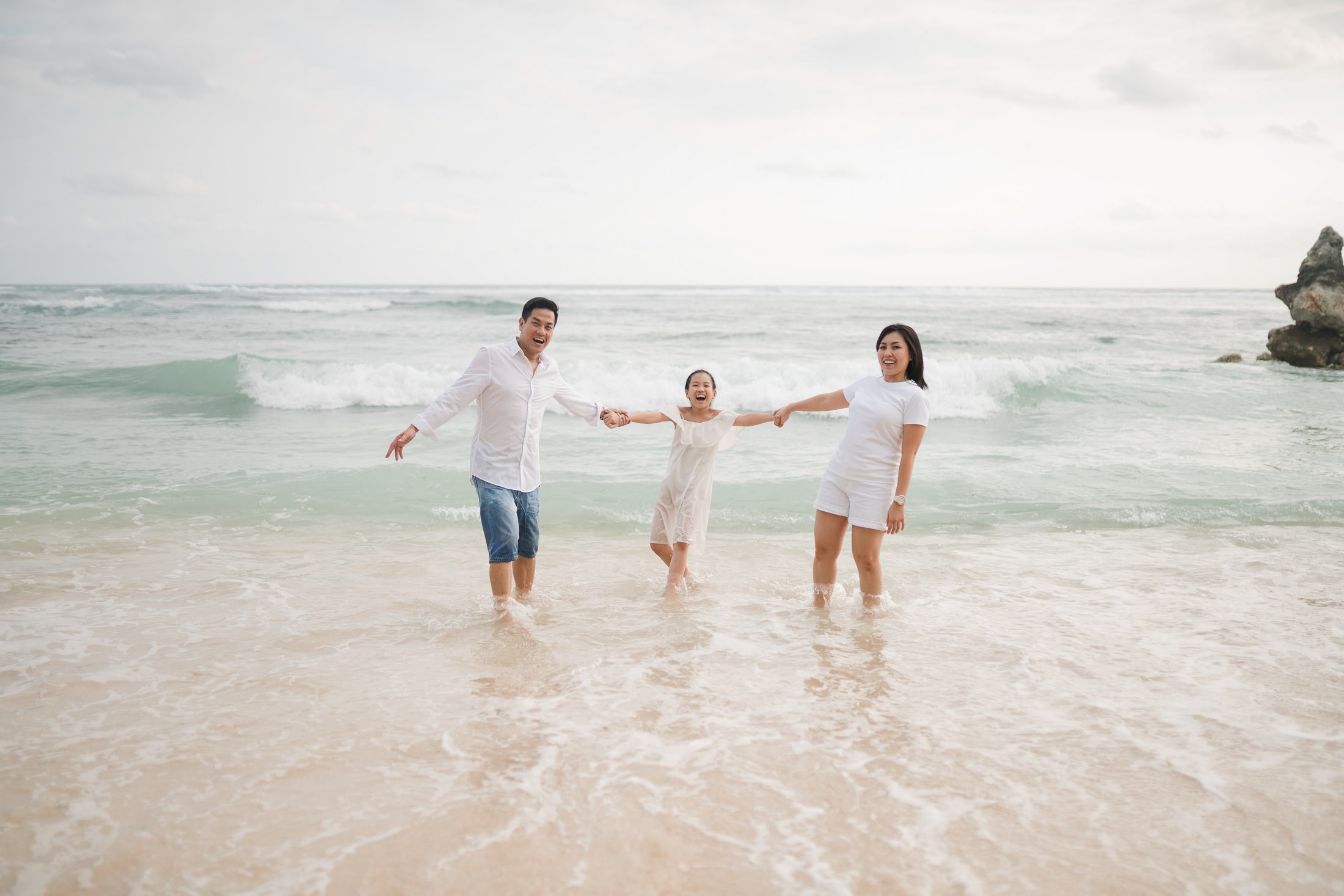 Family walking together through shallow ocean water at Melasti Beach Bali during a relaxed family photoshoot