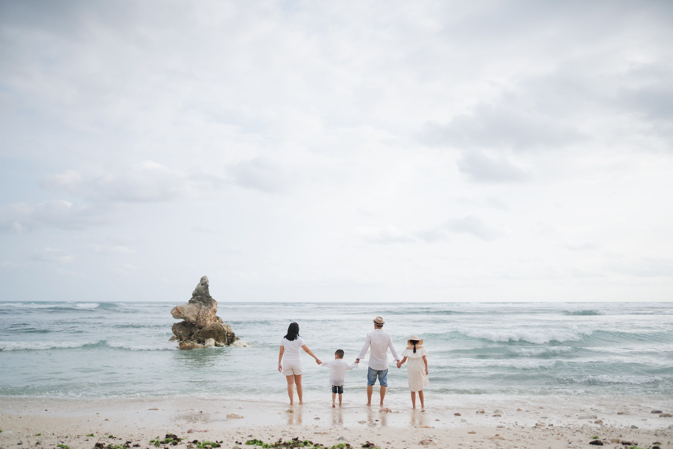 Family standing together facing the ocean at Melasti Beach Bali during a scenic beach photography session