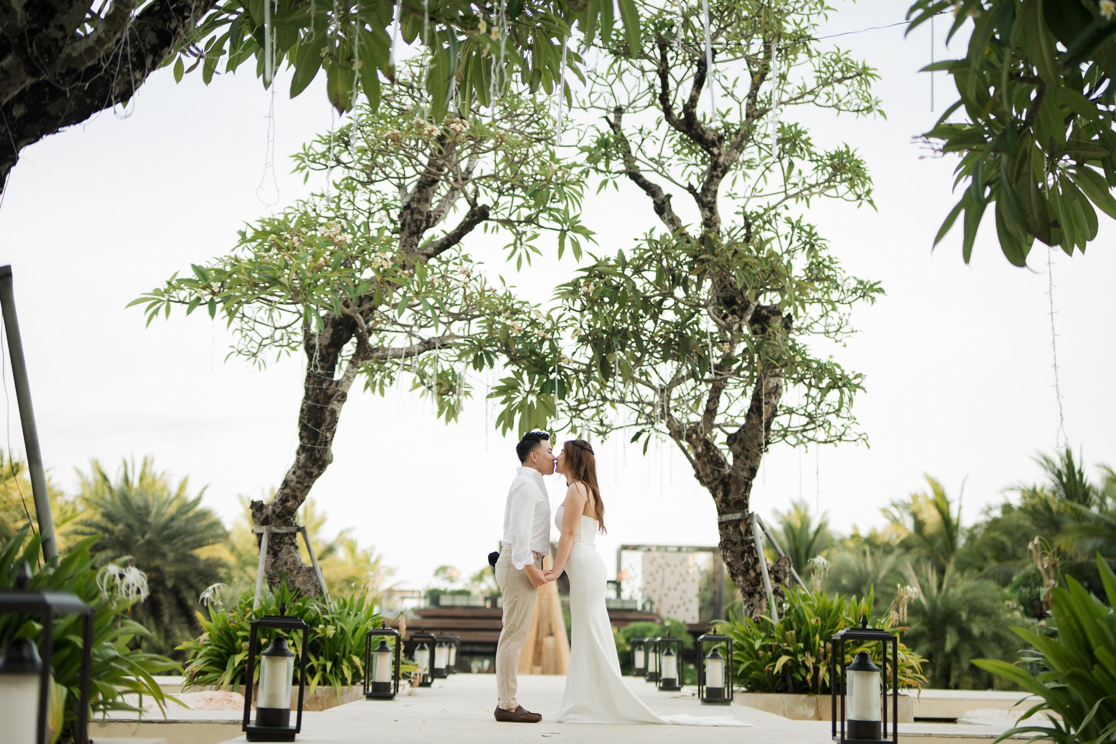 Couple standing under tropical trees during a romantic prewedding photoshoot at Apurva Kempinski Bali