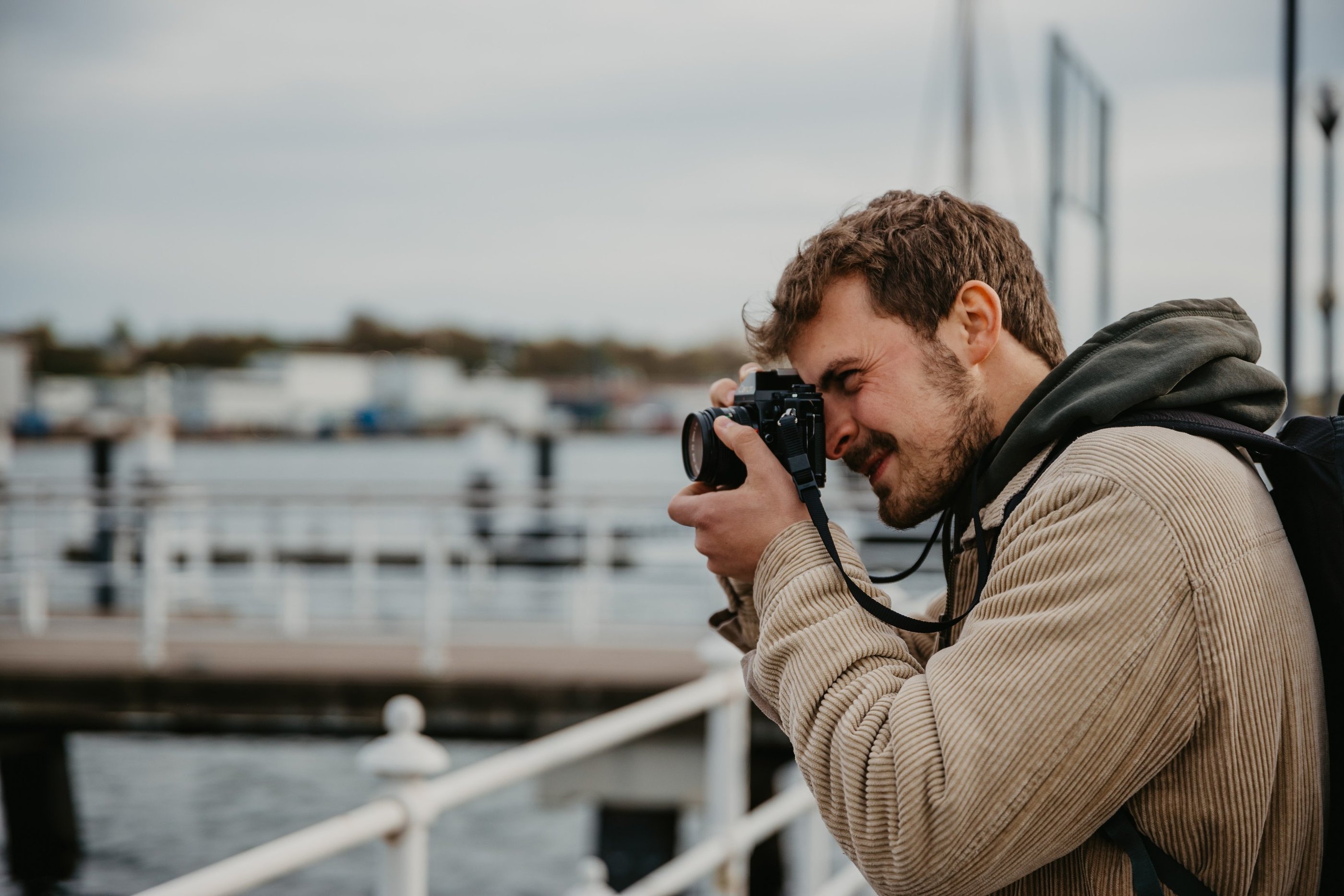 A male photographer taking a picture with a professional camera at a scenic waterfront harbor.