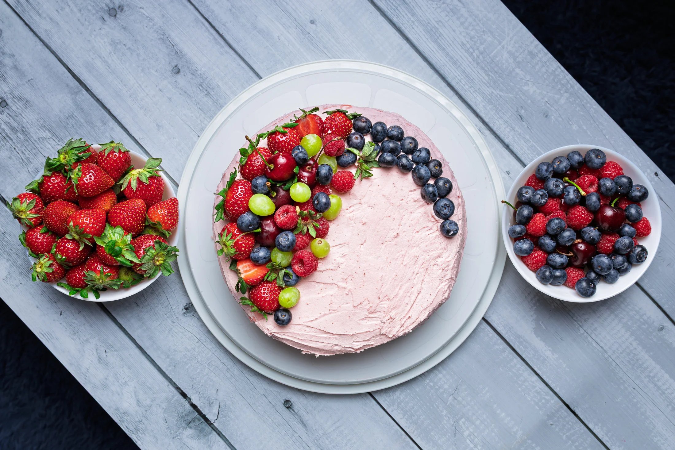 a cake with fruit on a table with bowls of fruit