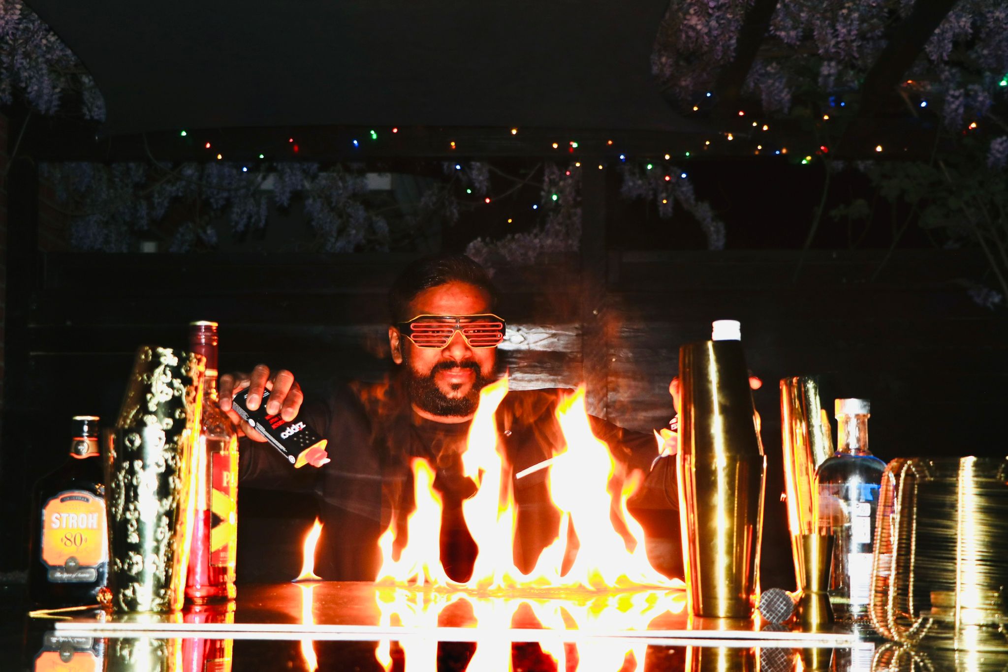 Professional mixologist performing a fire show with flames on a bar counter and cocktail shakers.