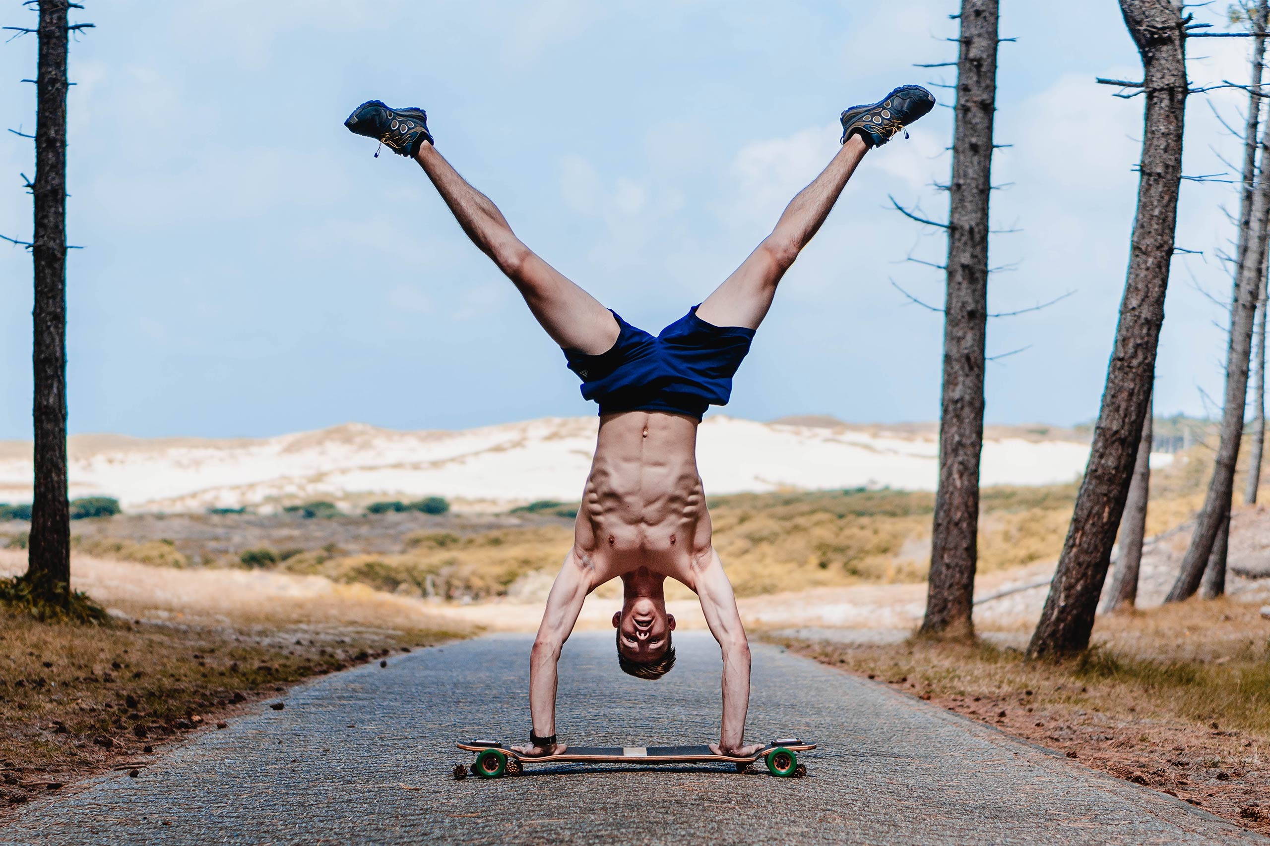 Mann macht Handstand auf einem Longboard auf einem Waldweg. Kreatives Sportfoto von Joel Pingel.