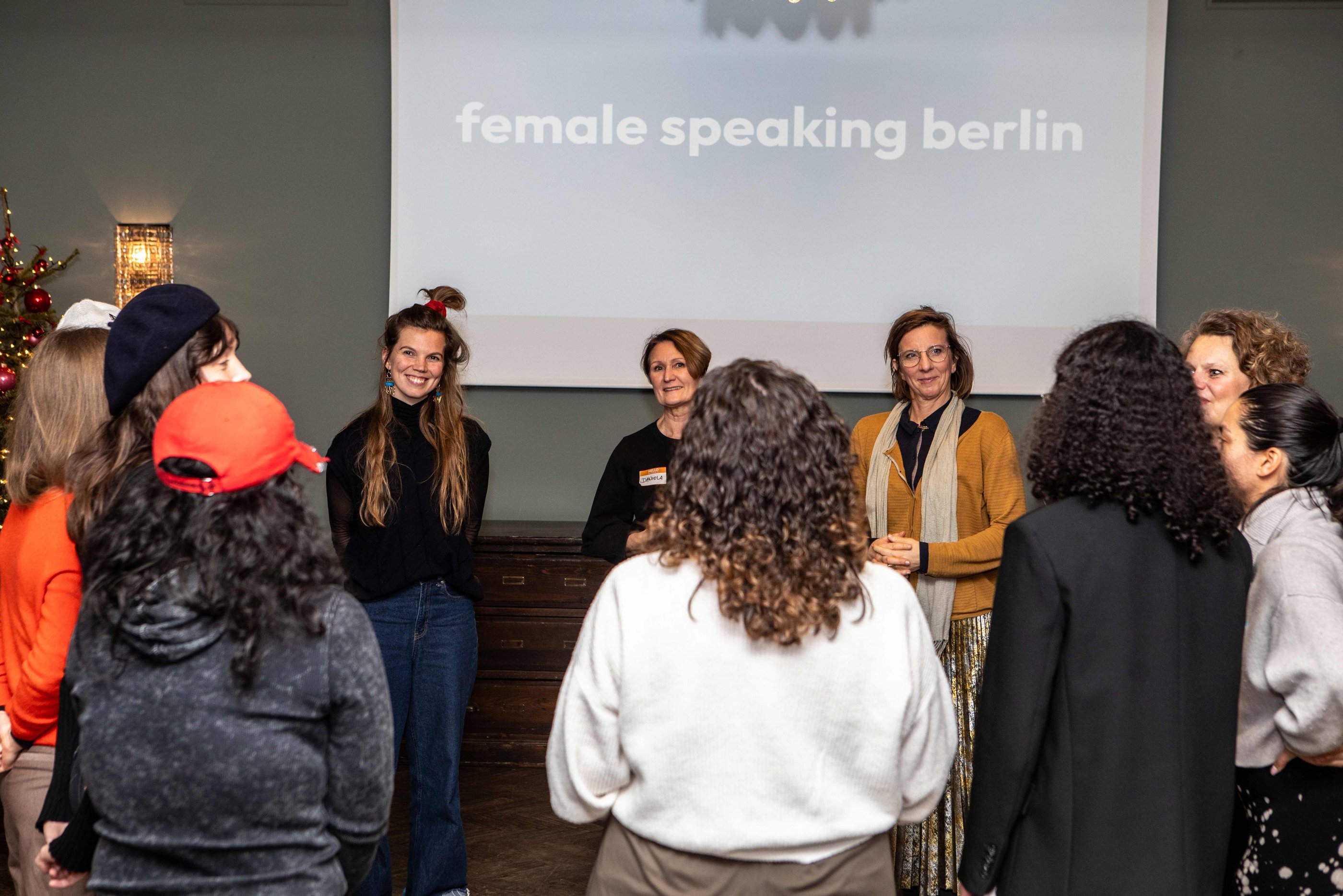 Women in circle, smiling and listening to each other, in workshop room, beamer logo female speaking 