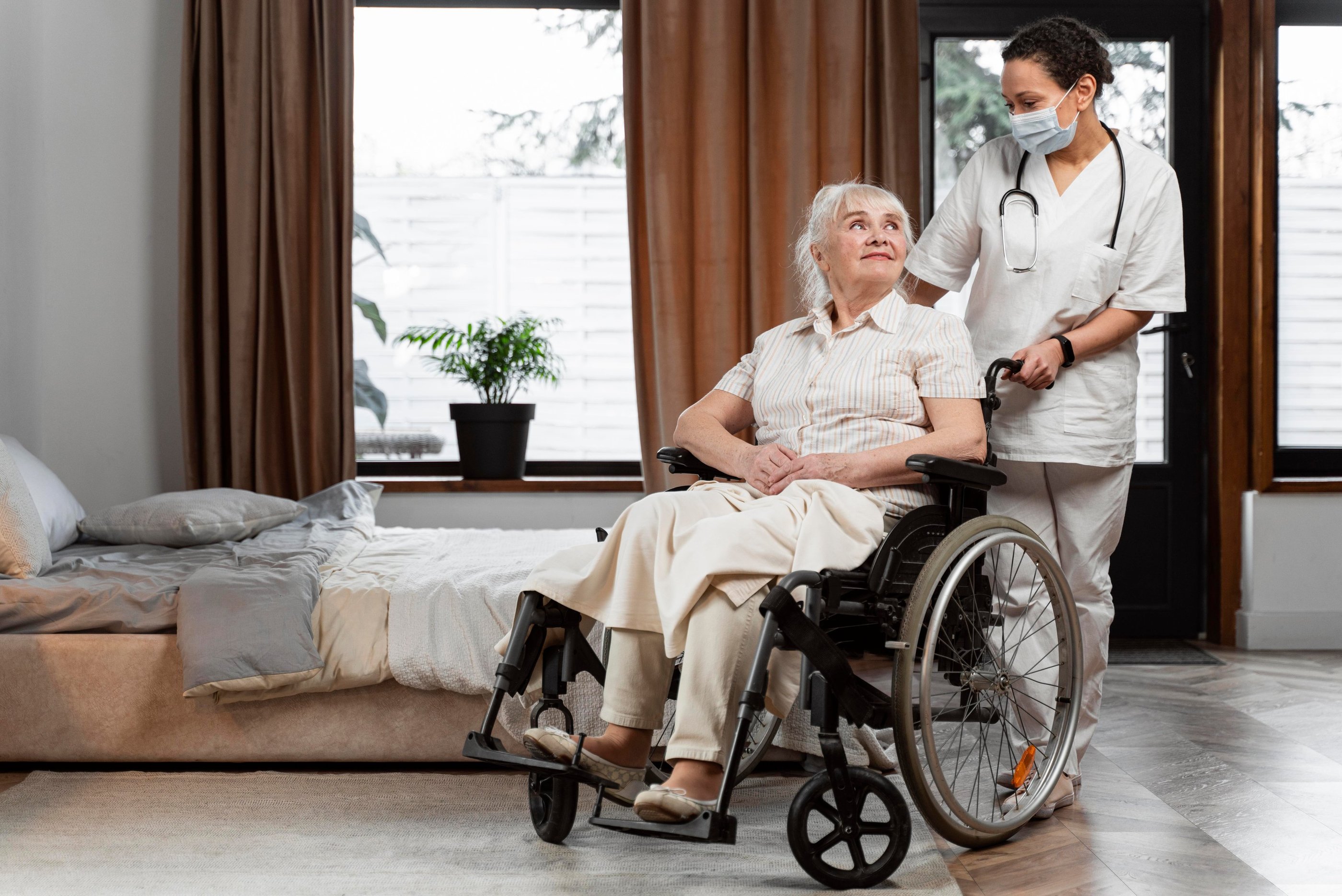 A female nurse in a face mask assisting a senior woman in a wheelchair during home health care.