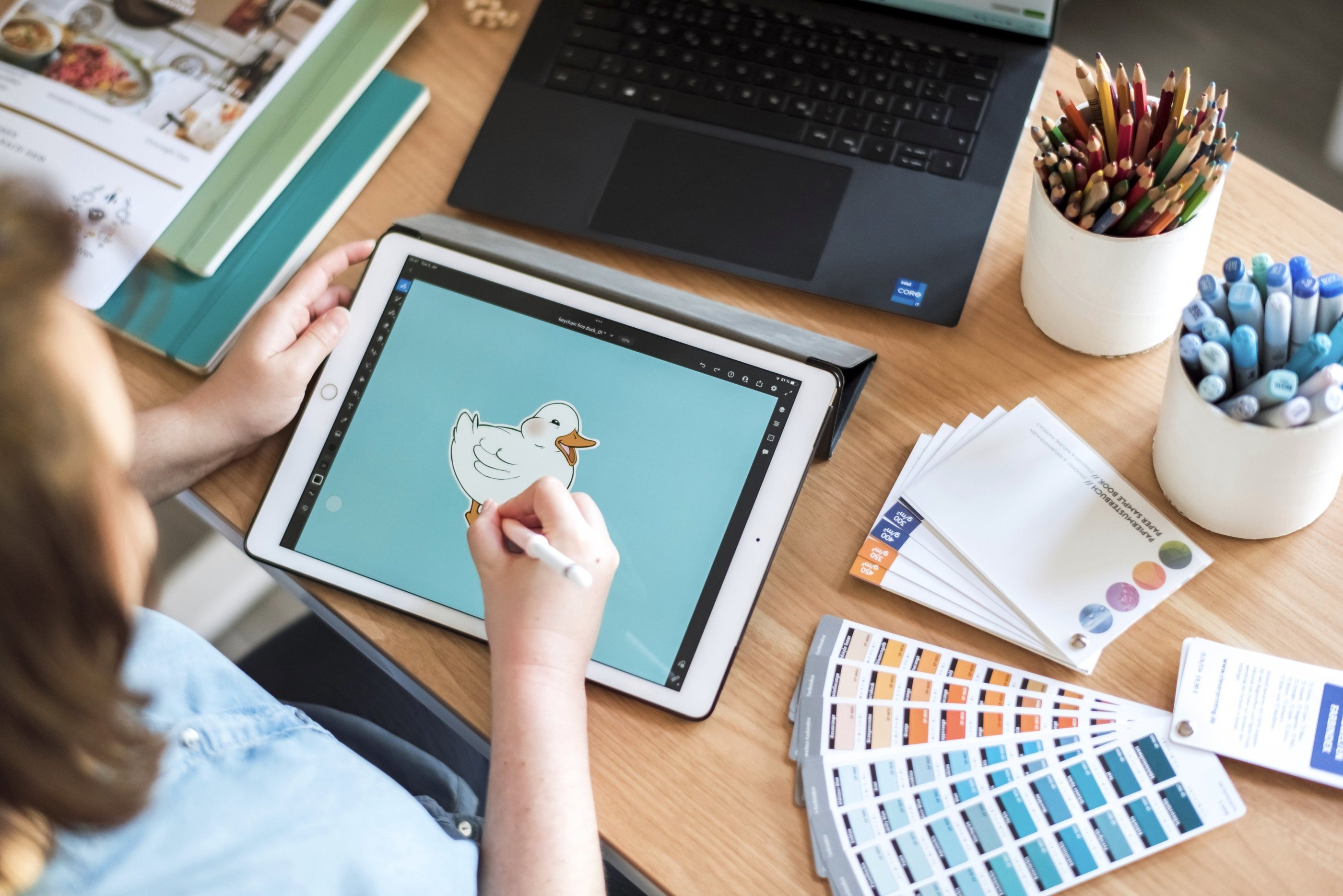 Arbeitsplatz mit Laptop, iPad, Farbkarten und Papierproben.