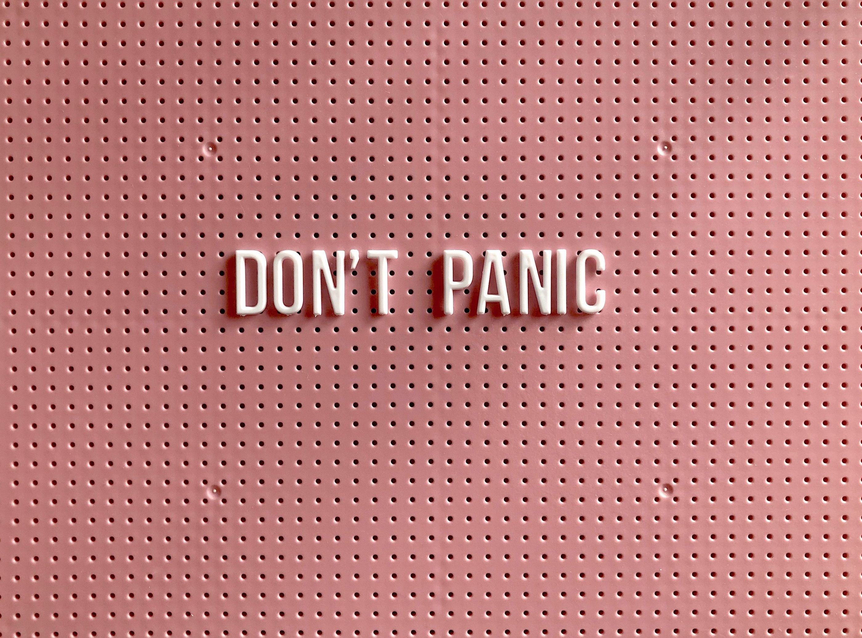 White 3D letters spelling Don't Panic on a textured pink pegboard background.