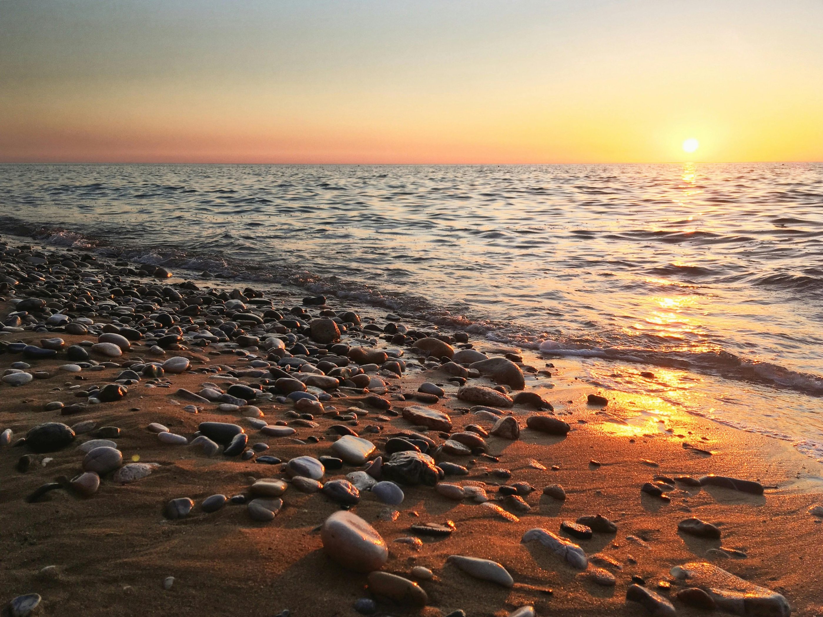sand and pebble beach with sun setting over the calm sea