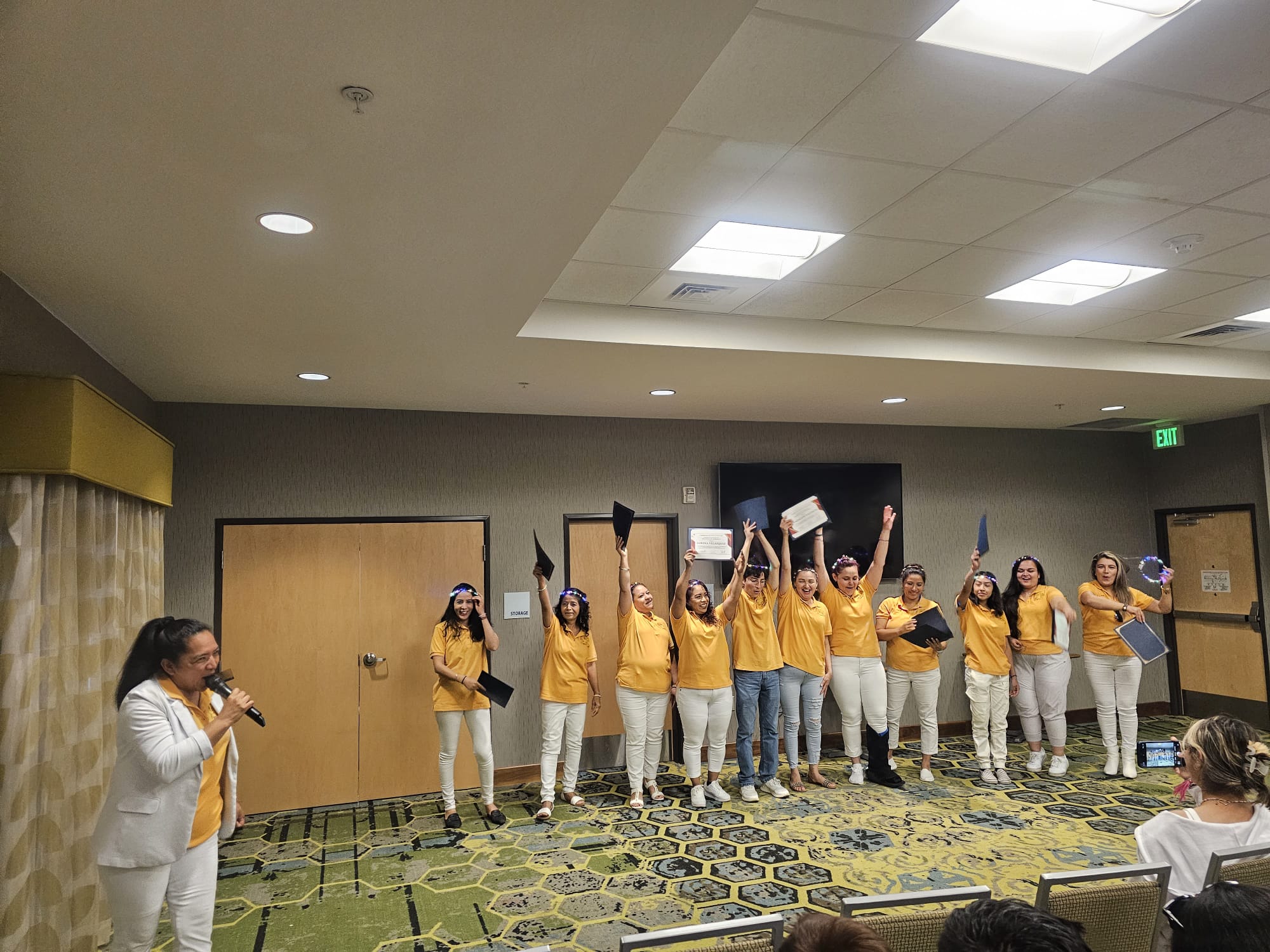 Smiling graduates in yellow shirts hold up diplomas during a celebratory graduation ceremony.