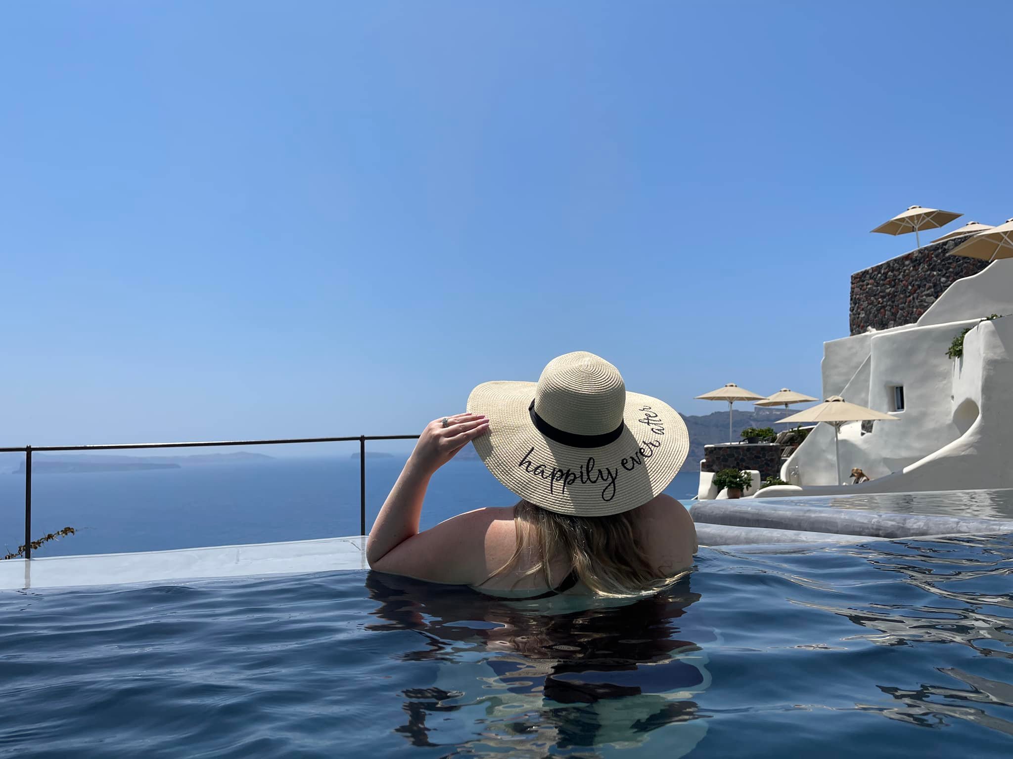The back of a woman in a pool wearing a large sun hat 