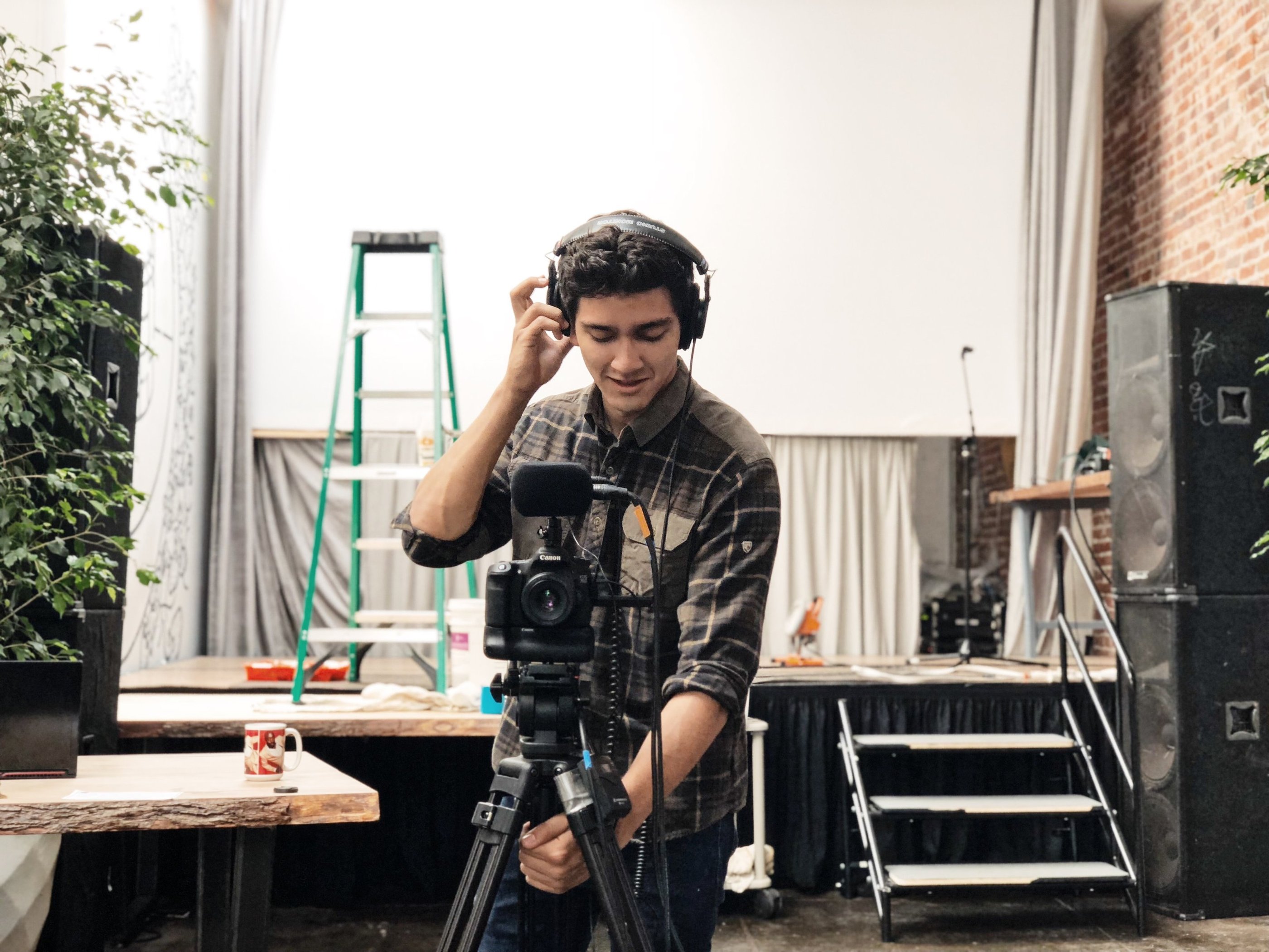 a man in a plaid shirt and headphones on a tripod recording video