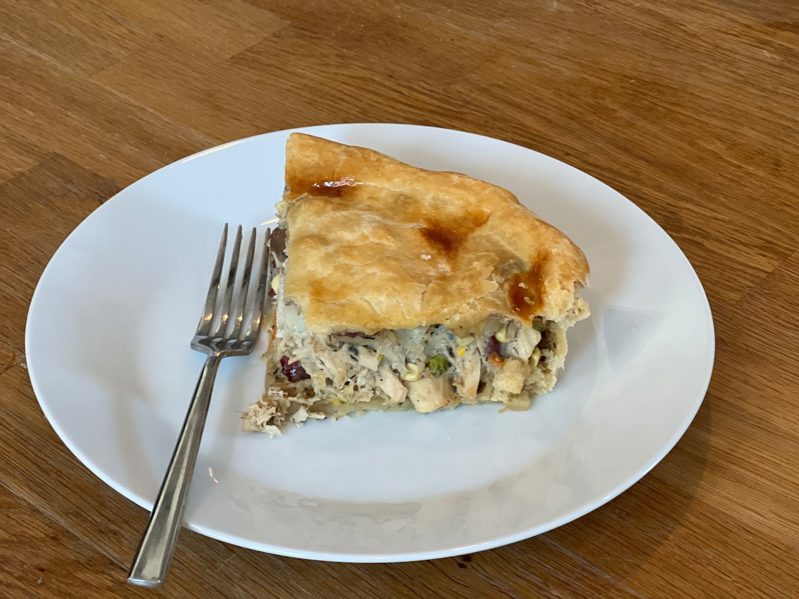 A slice of homemade savory chicken pot pie with a golden flaky crust on a white plate with a fork.