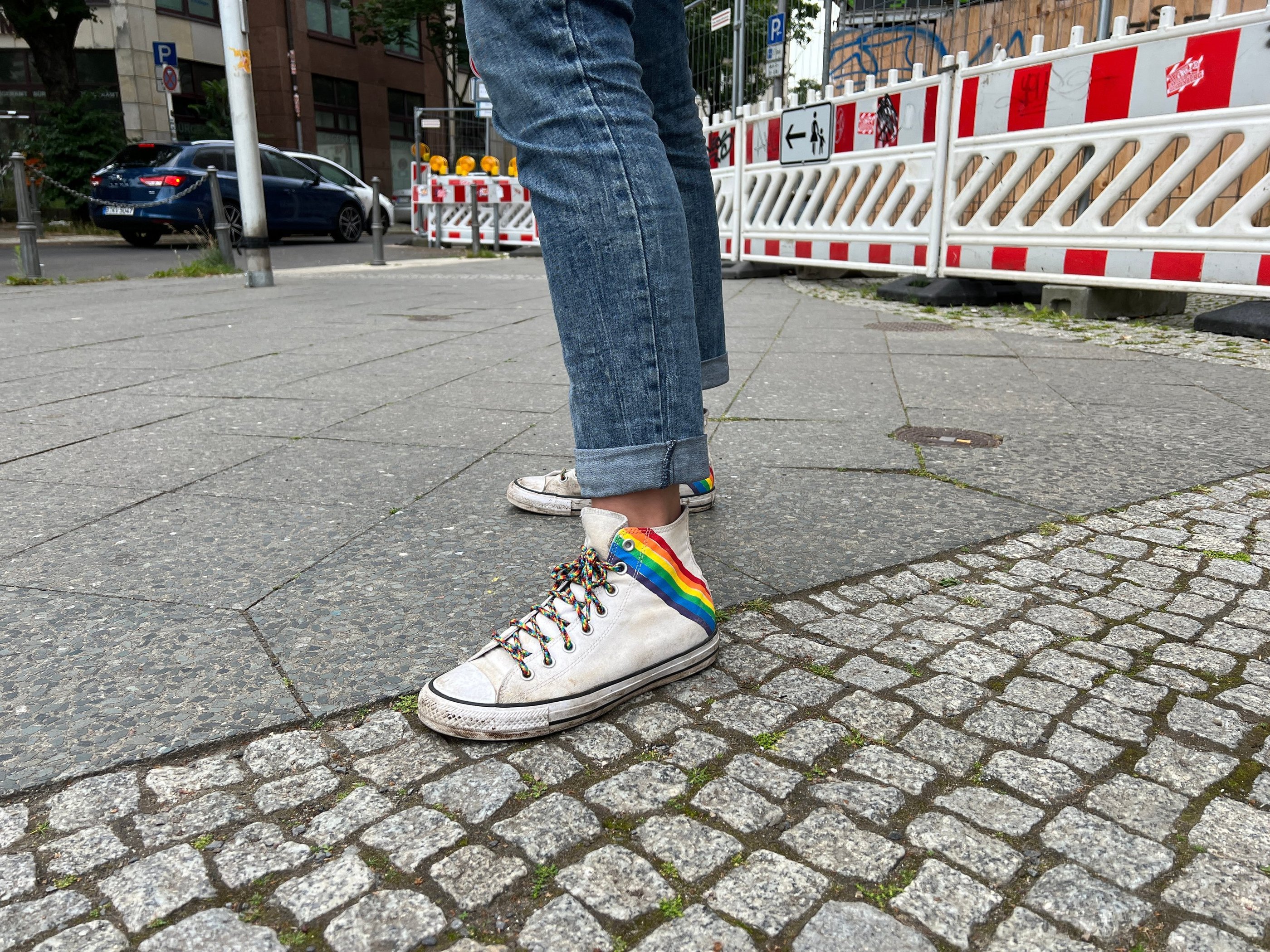 Foto von weißen Turnschuhen mit Regenbogenaufdruck und Regenbogenschnürsenkeln.