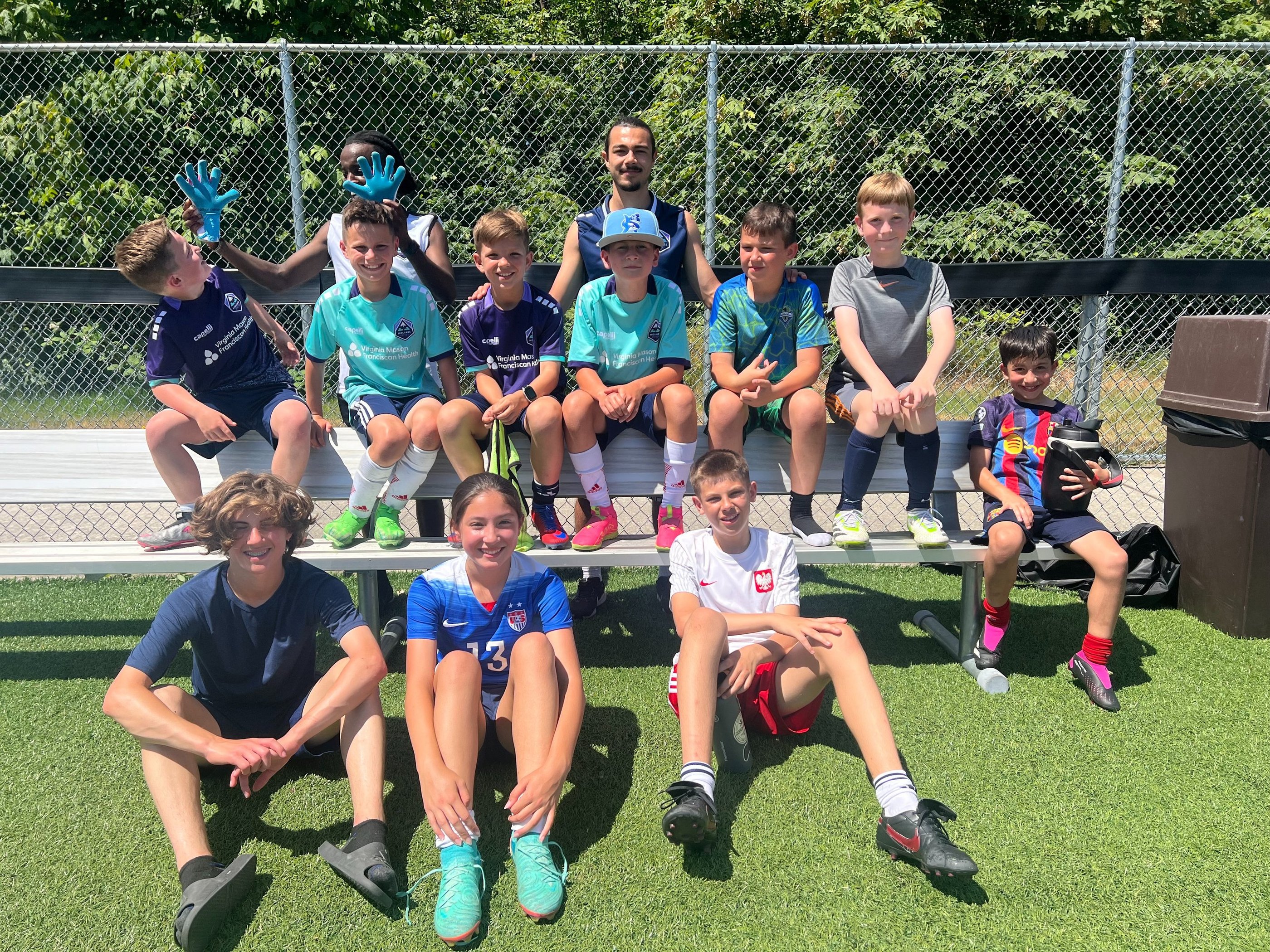 Kids from soccer camp sitting on a bench.