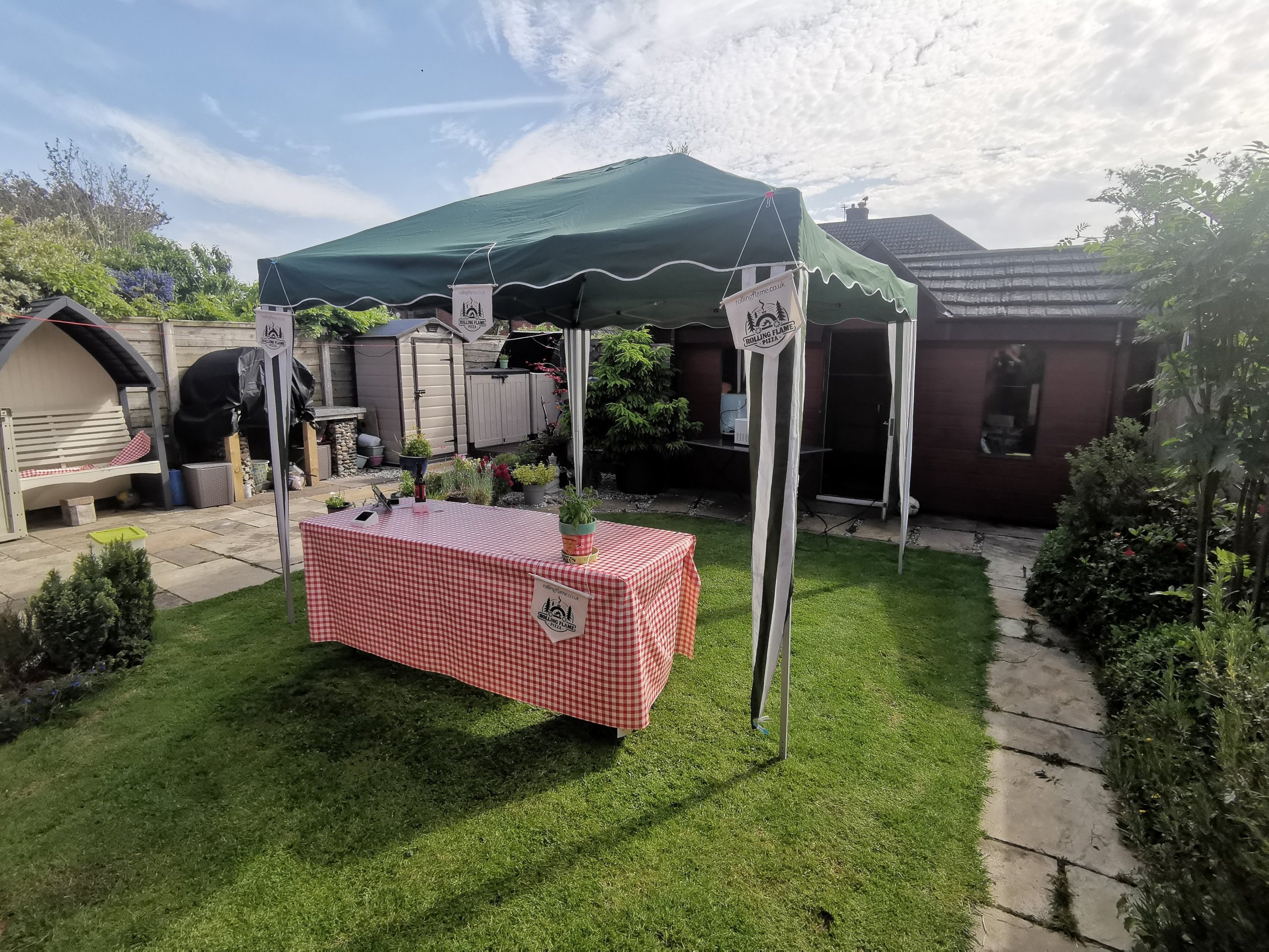 Green garden gazebo canopy and red gingham table set up for an outdoor backyard party on a sunny lawn.