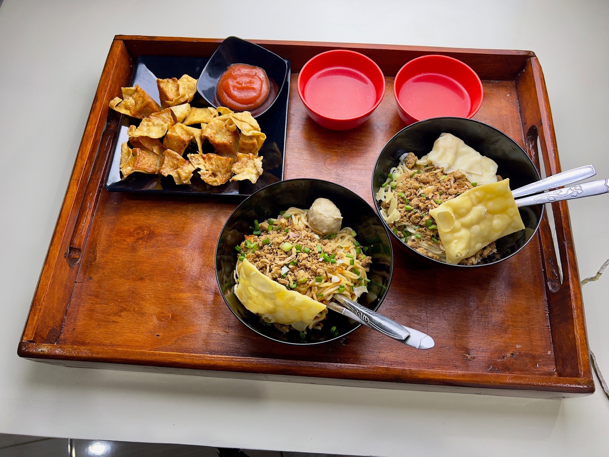 Tray berisi dua mangkuk mie ayam dengan topping lengkap, dua mangkuk saus, dan pangsit goreng
