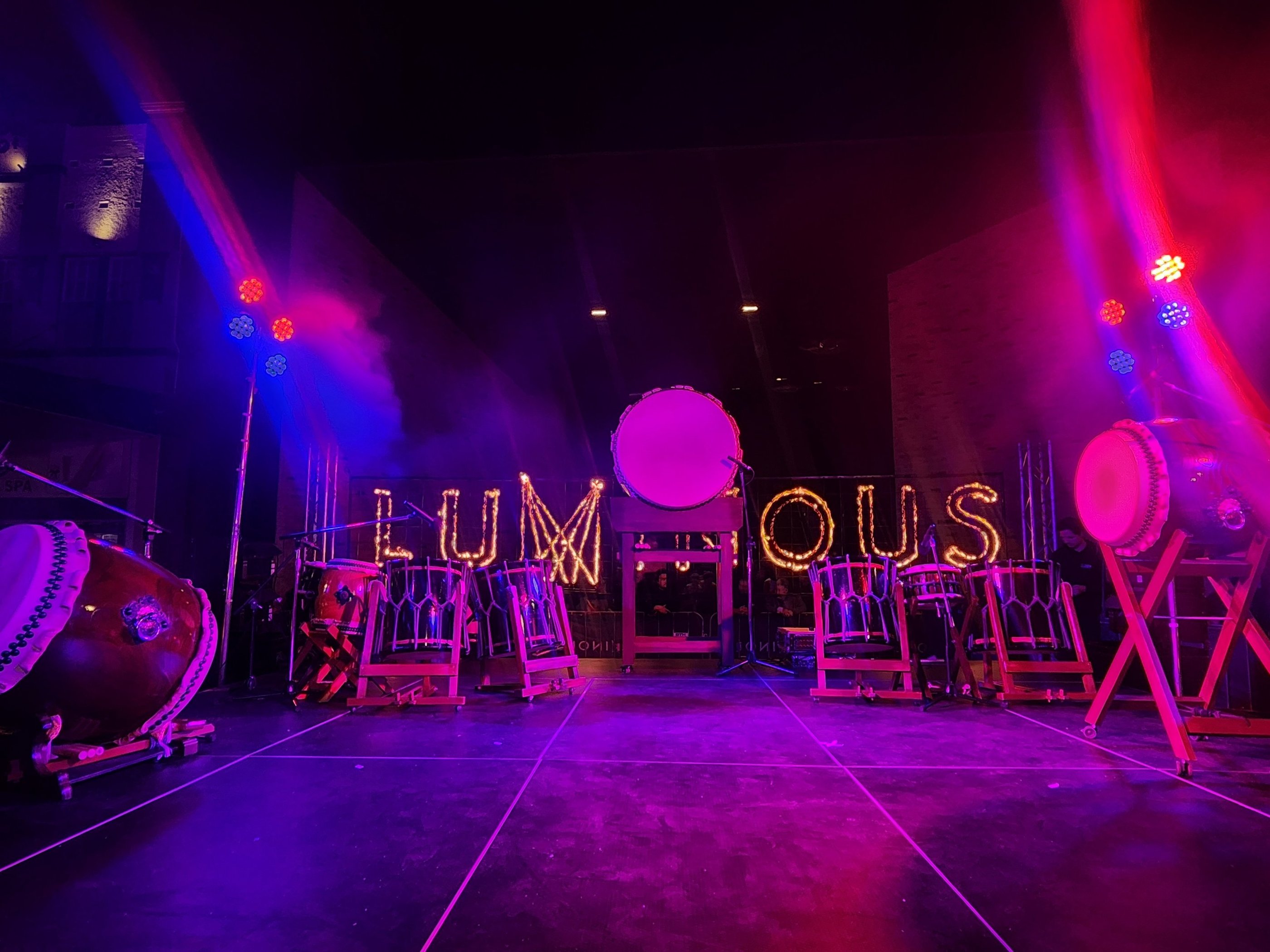 Traditional Japanese Taiko drums on a stage with purple neon lighting and a glowing Luminous sign.