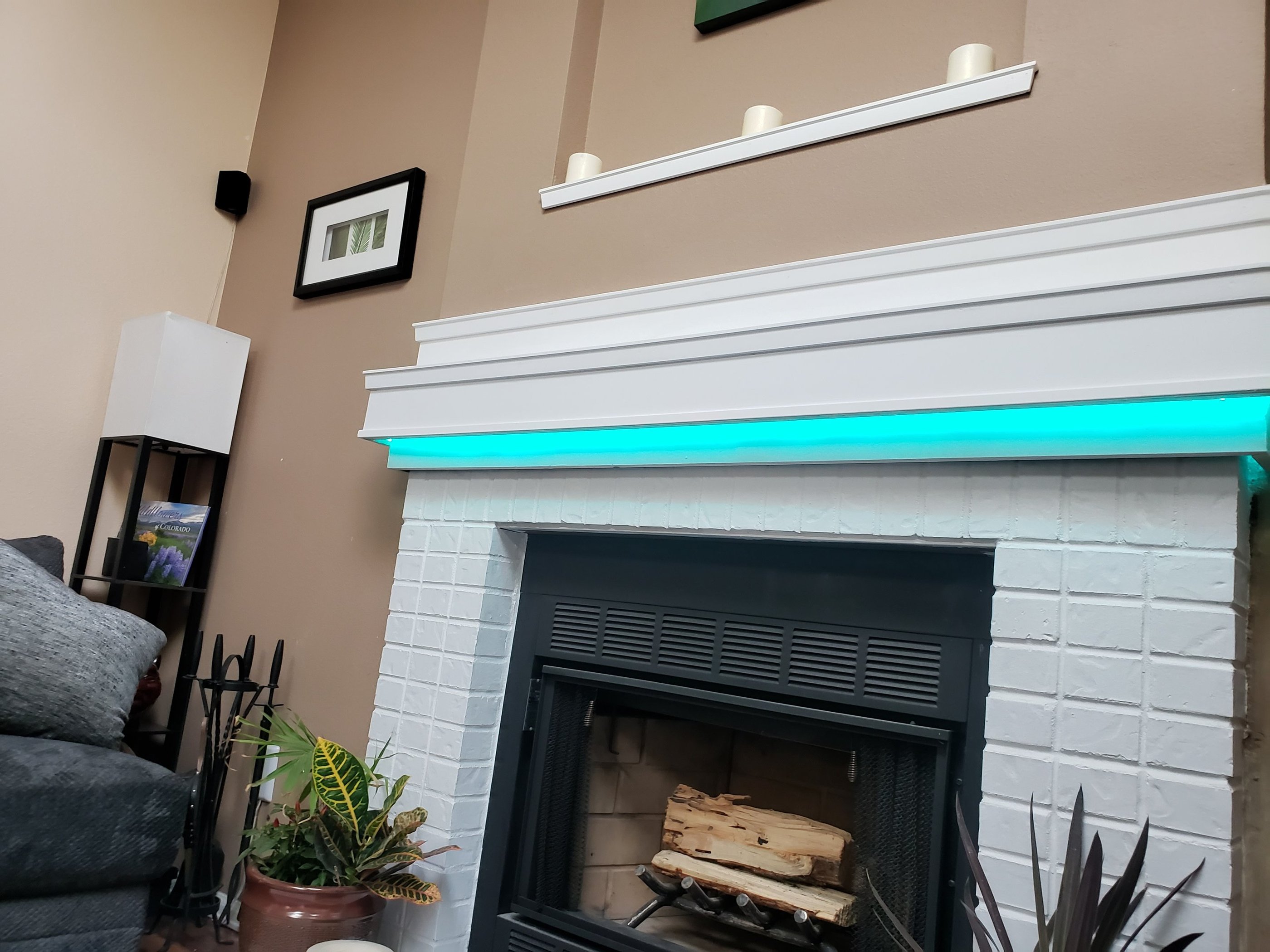 Modern white brick fireplace featuring a turquoise LED light strip under the mantel in a cozy living room.
