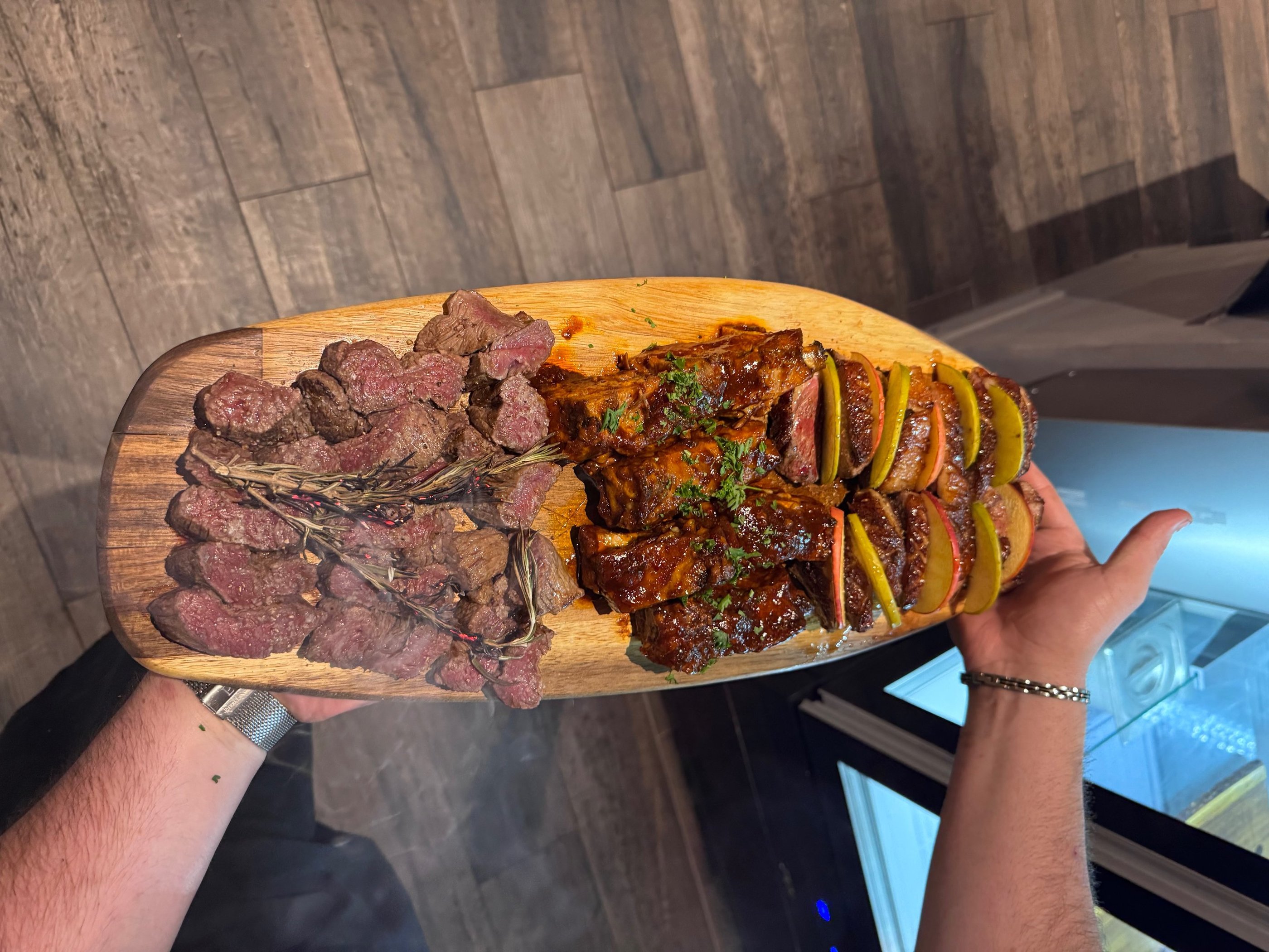 a person holding a large wooden board with steak steak and potatoes