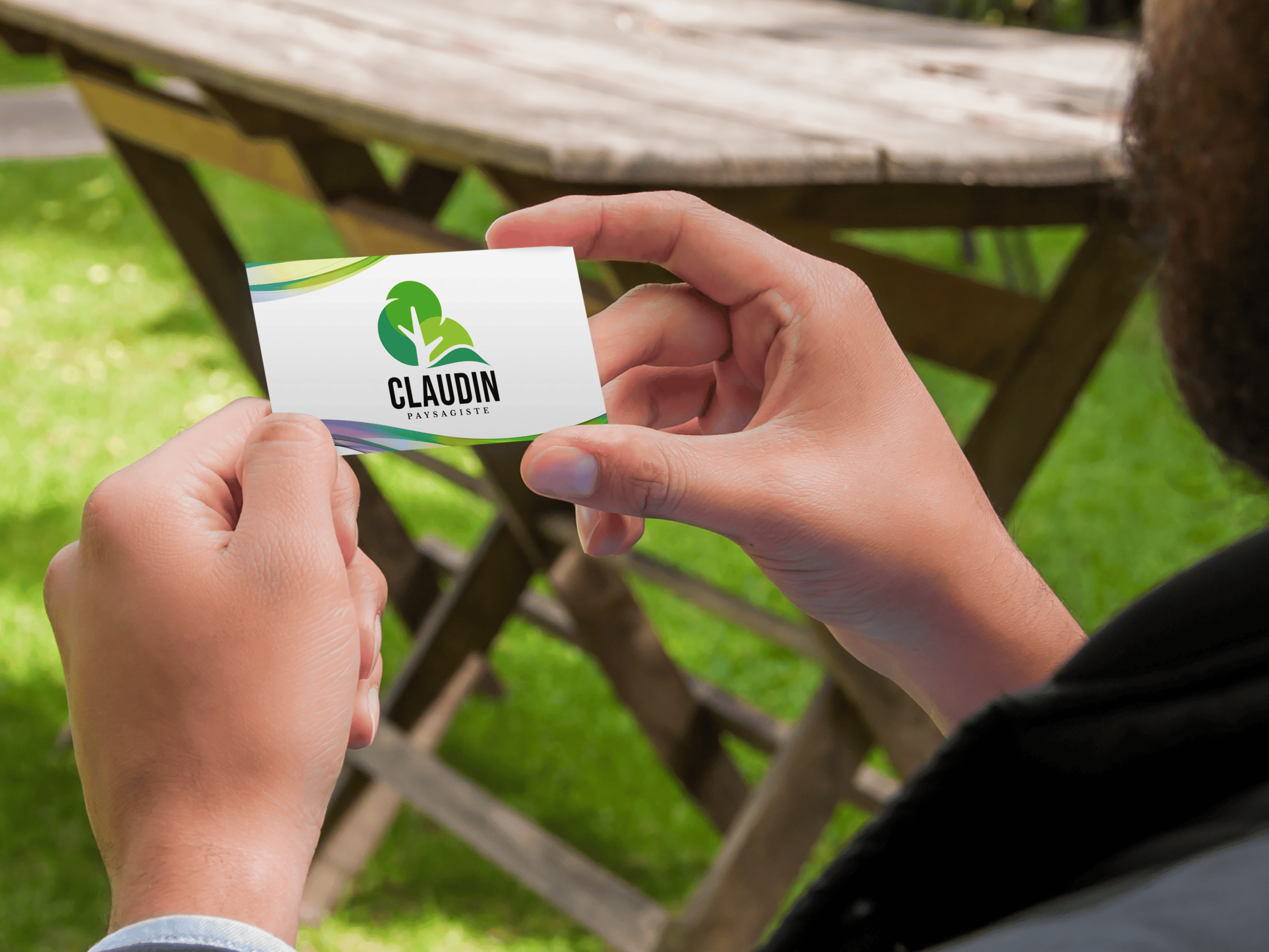 Une personne tient une carte de visite de paysagiste avec un logo d'arbre vert à l'extérieur.