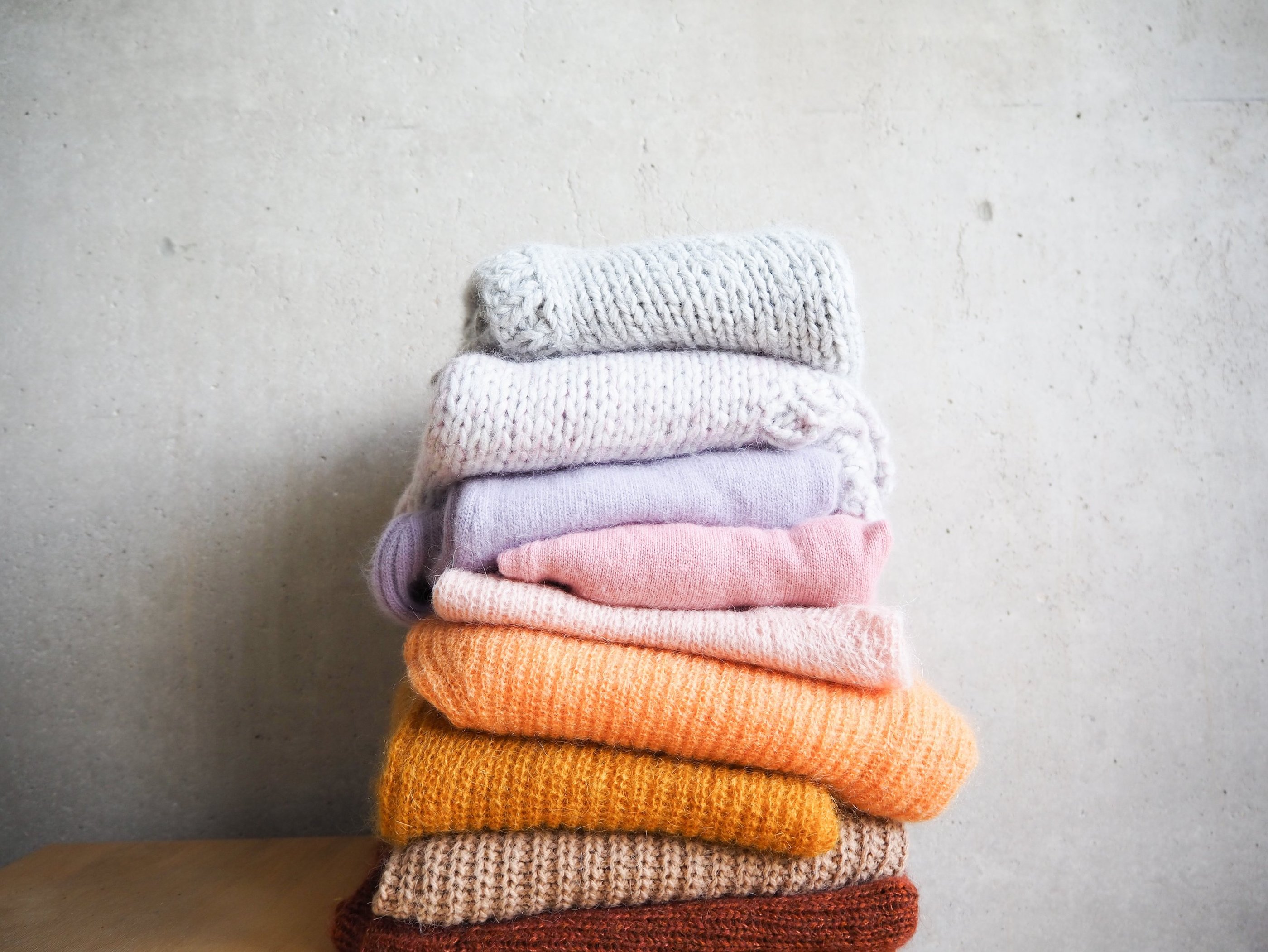 wełniane swetry ułożone w stos na tle szarej ściany