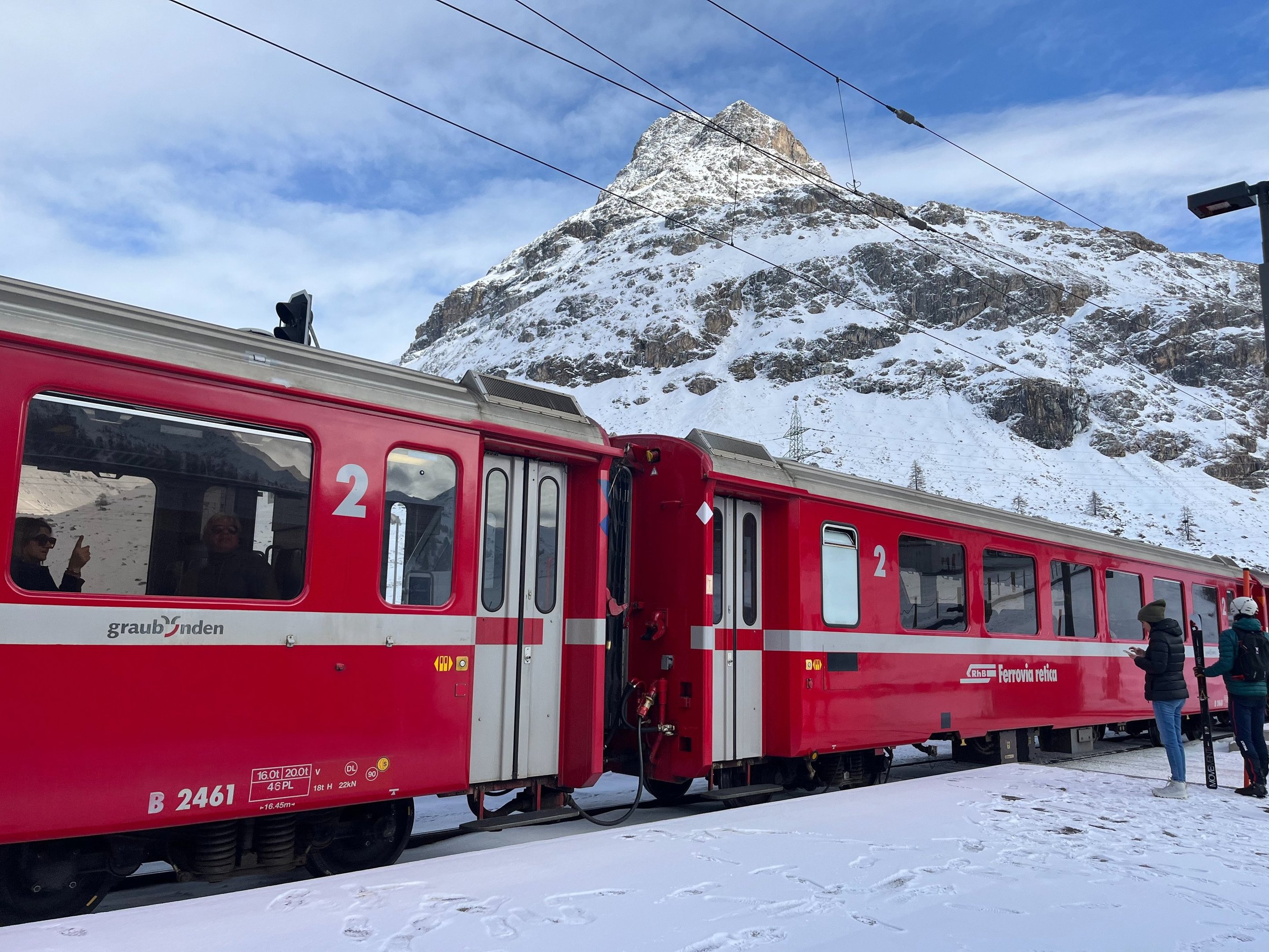 Two red Rhaetian Railway train cars in front of the mountains at Bernina Pass in Switzerland