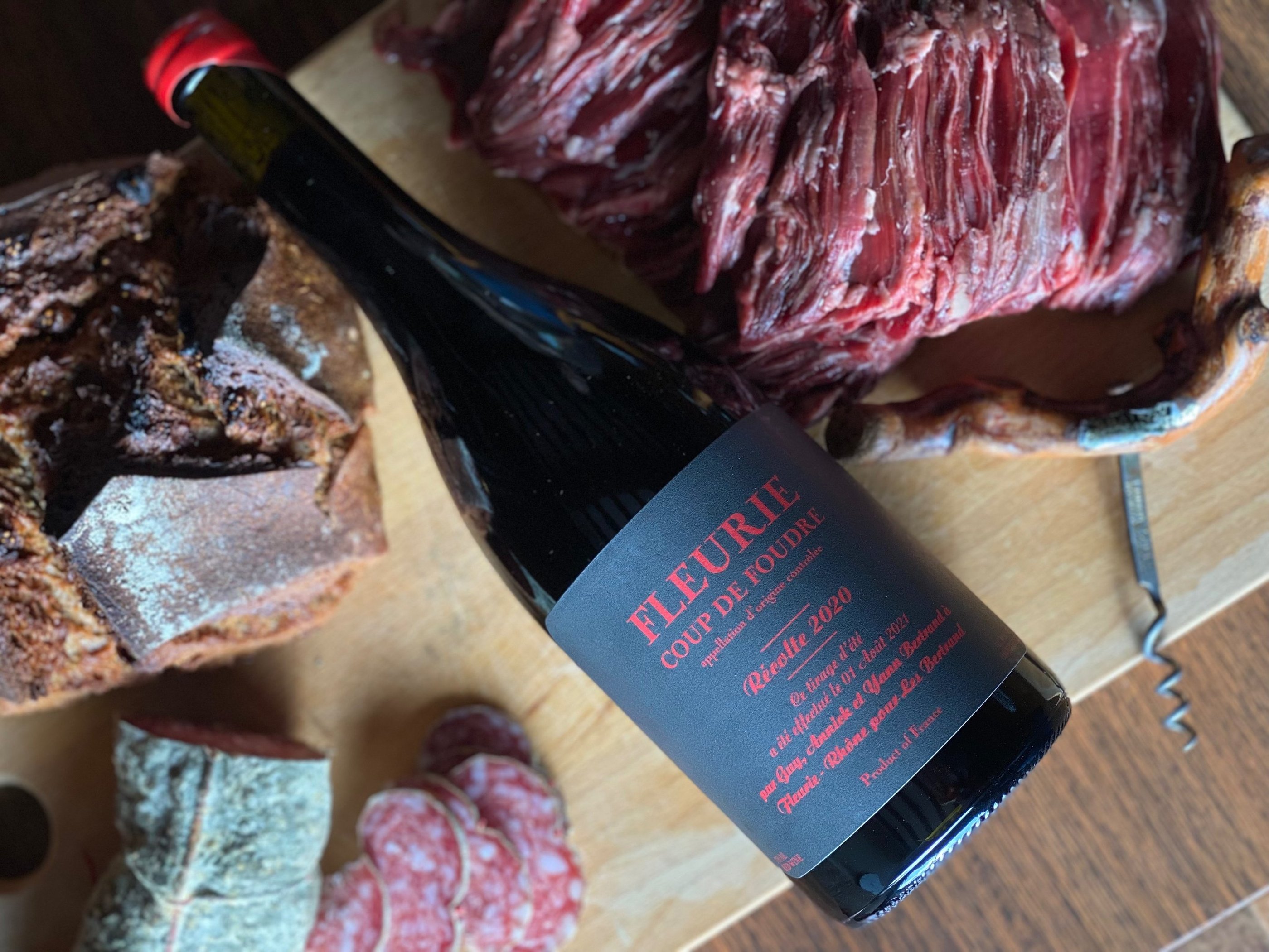 Une bouteille de vin rouge, du pain, de la viande et du saucisson sur une planche en bois.