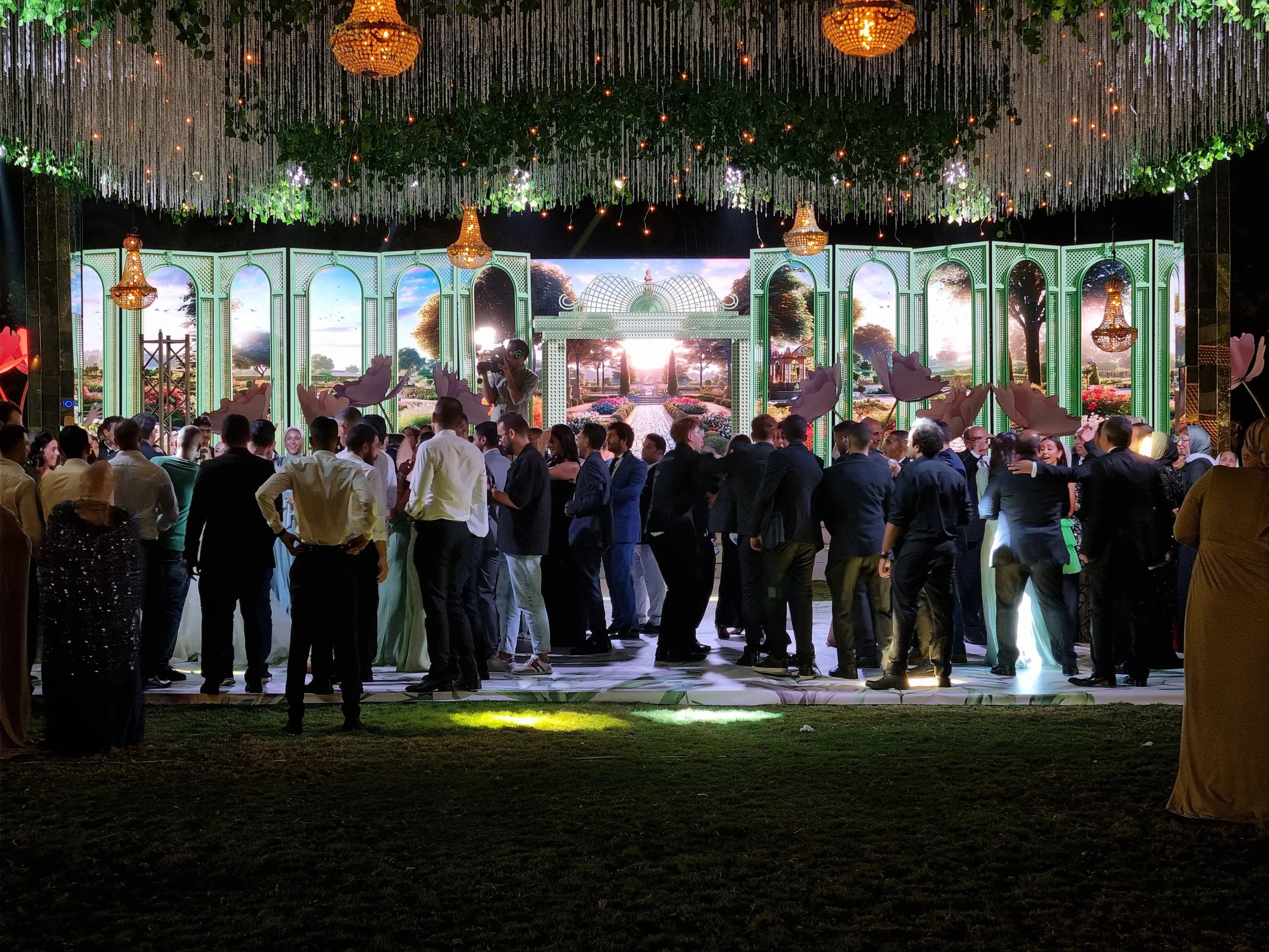 a group of people standing on a stage in front of wide led screen with garden scenery on it