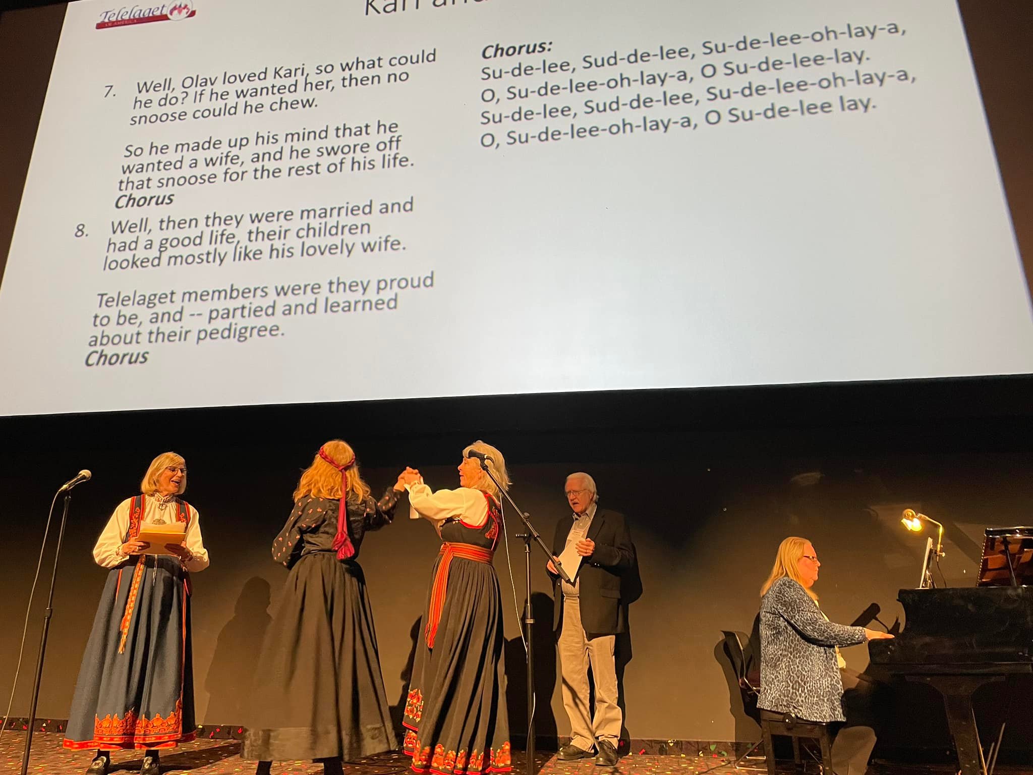 a woman in bunad singing, a man singing and two women in bunad dancing