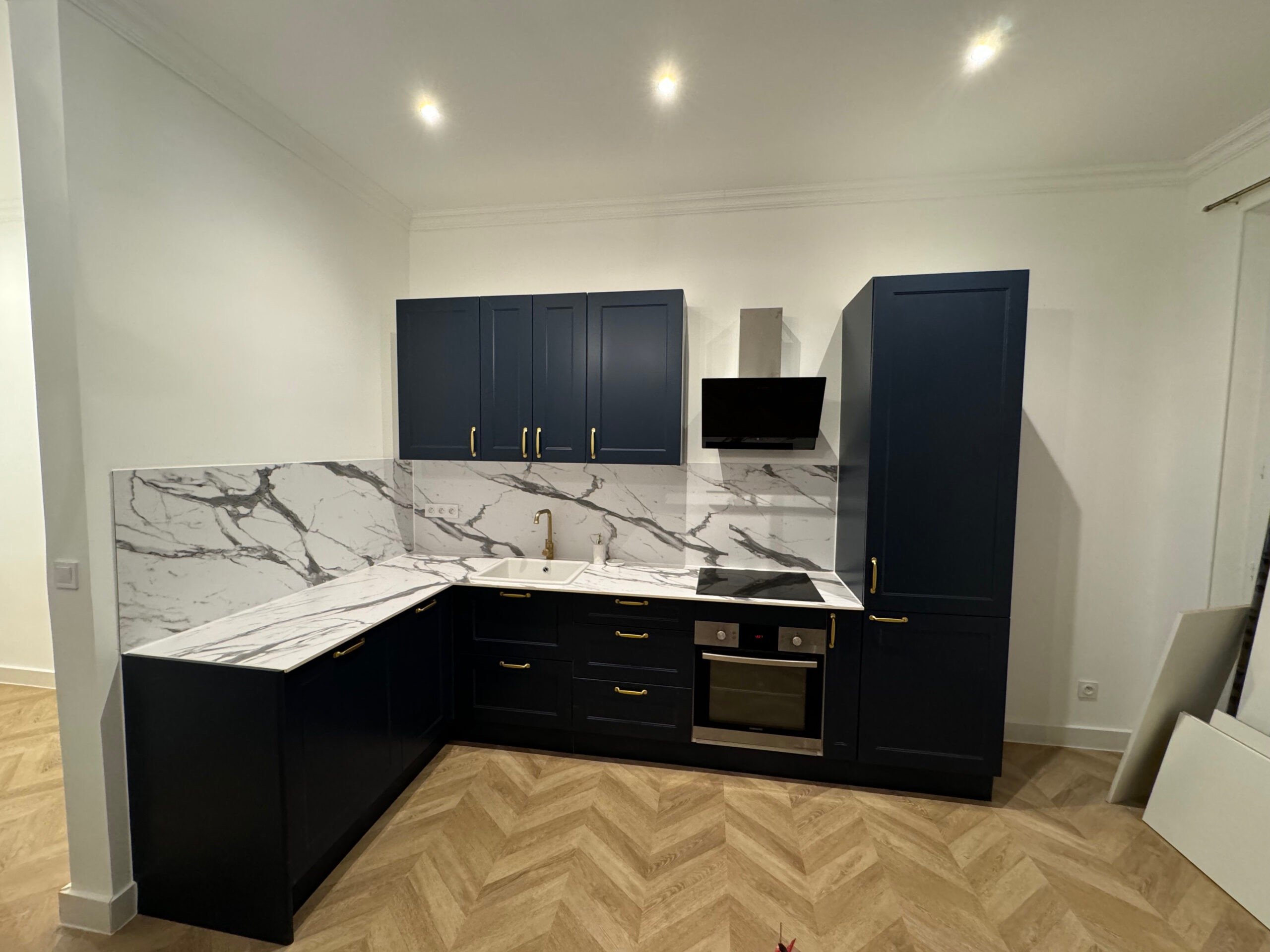  Réalisation d'une cuisine équipée avec plan de travail en marbre, meubles noirs et parquet chevron. Harenova