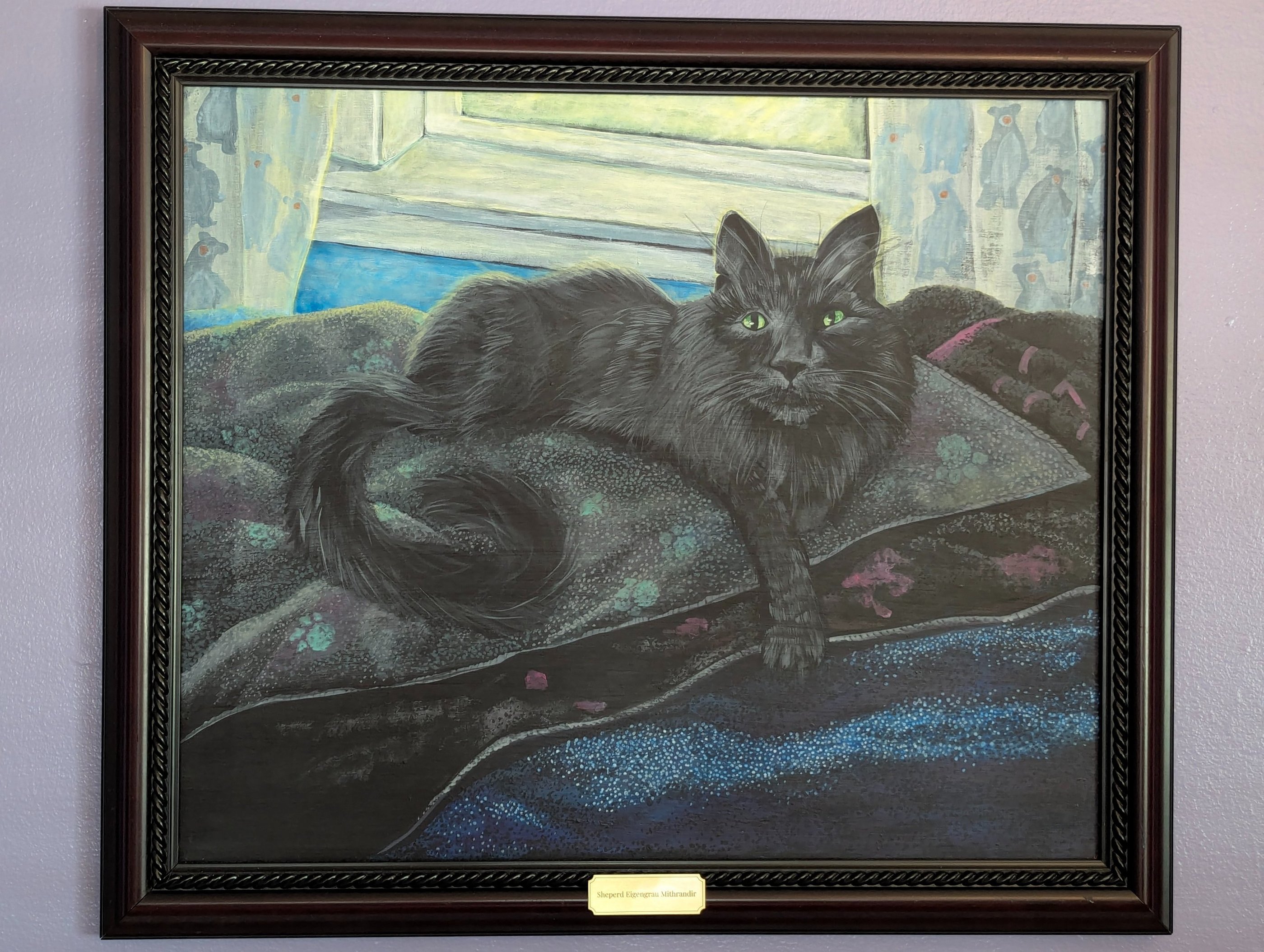 Framed painted portrait of a black long hair cat lounging in front of his window on his bed of blankets.