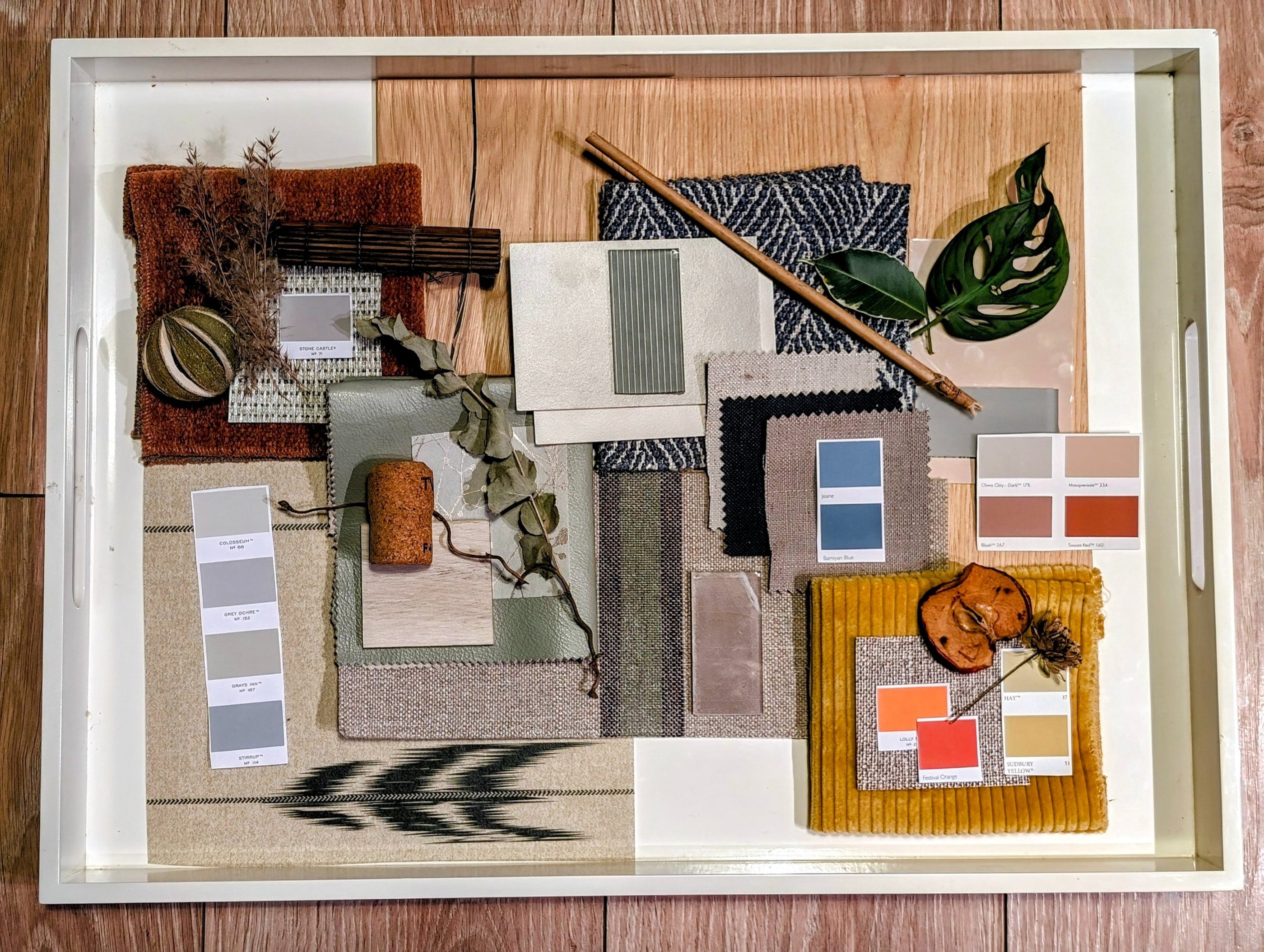 Interior design mood board on a white tray featuring fabric swatches, color palettes, and natural textures.