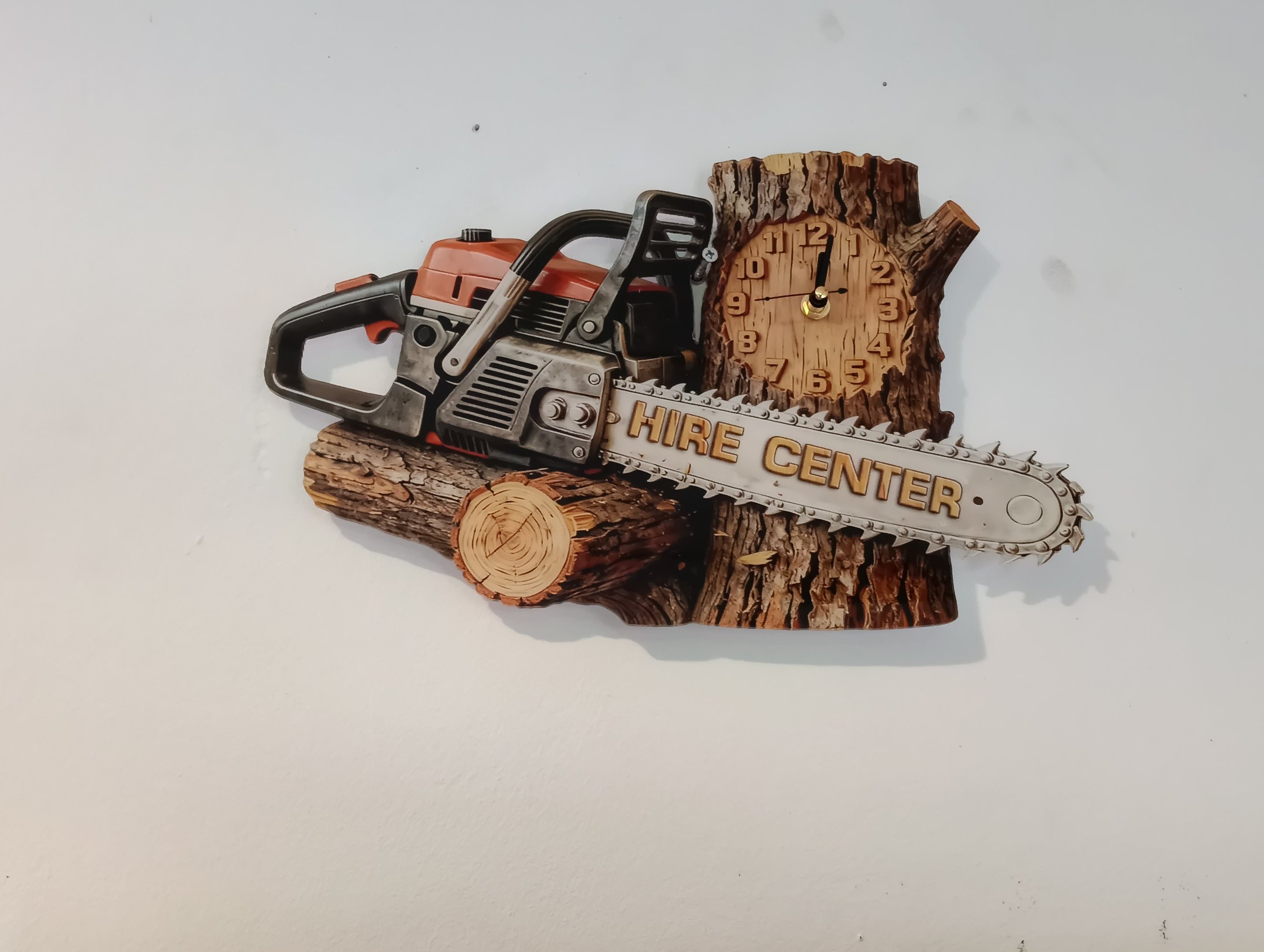 Rustic chainsaw wall clock carved into a wooden log featuring a Hire Center advertisement blade.