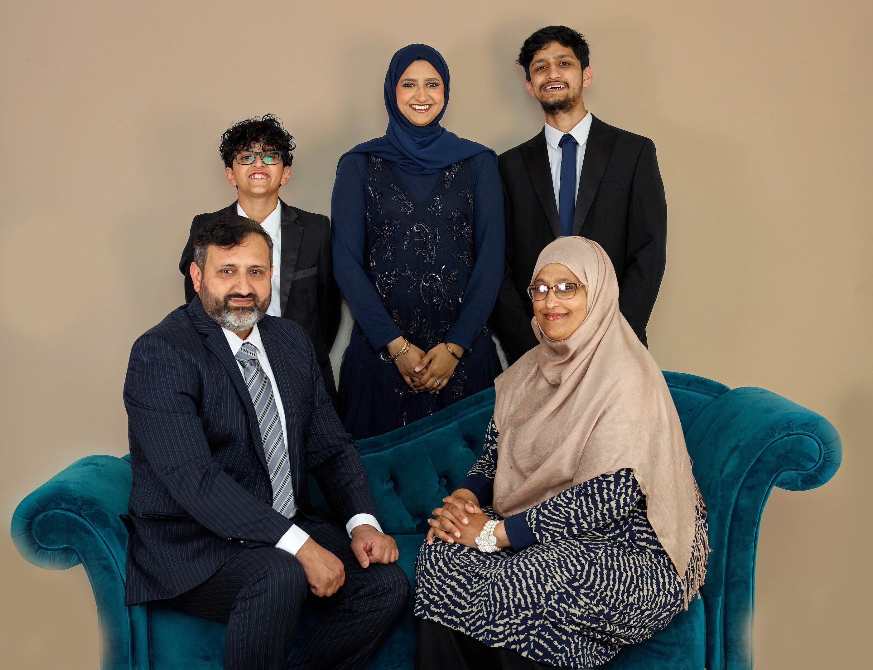 A smiling Muslim family in formal attire and hijabs posing for a studio portrait on a blue sofa.