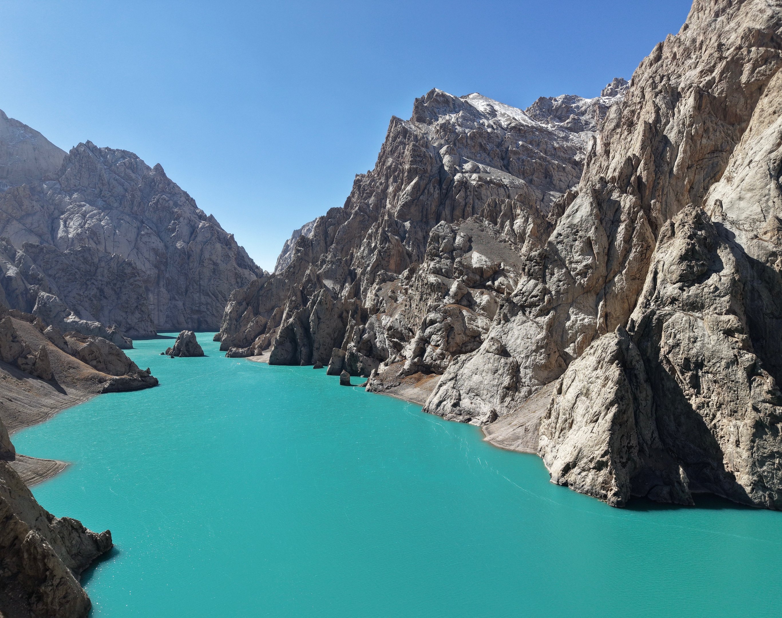 Turquoise alpine lake surrounded by steep, rocky mountain peaks under a clear blue sky.