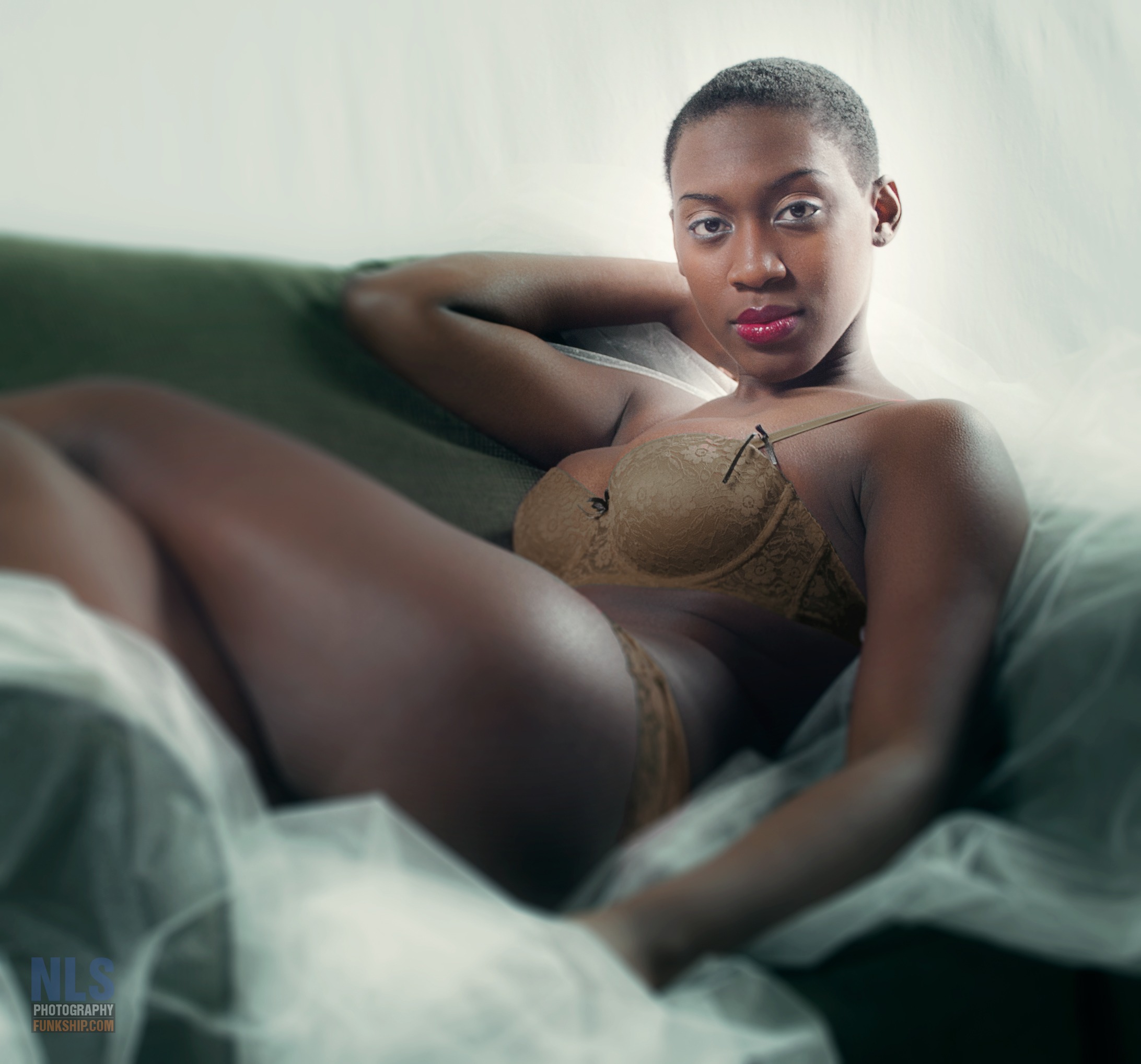 A confident woman posing in elegant brown lace lingerie on a green sofa.