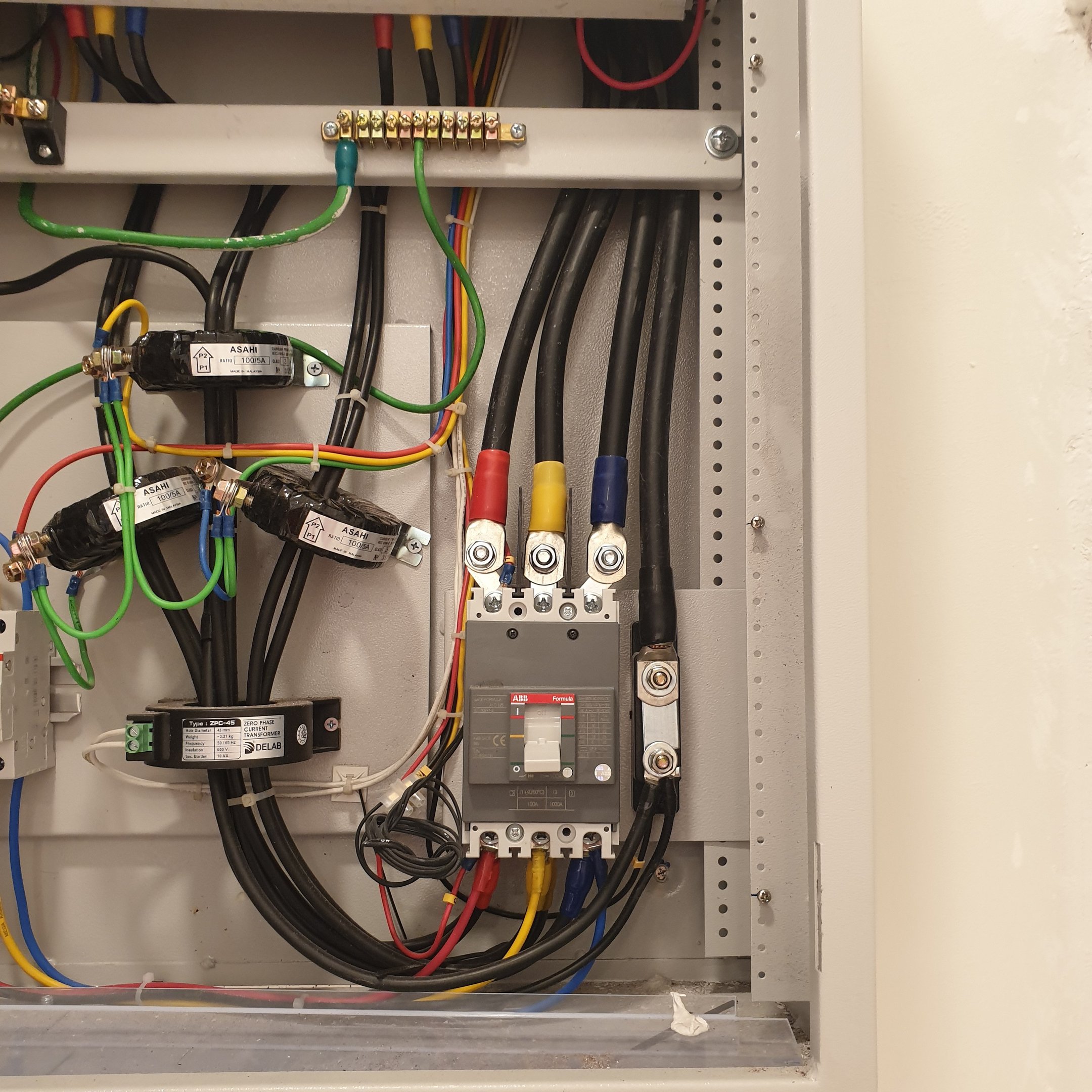 Industrial electrical panel with ABB circuit breaker, current transformers, and colored wiring for power distribution.