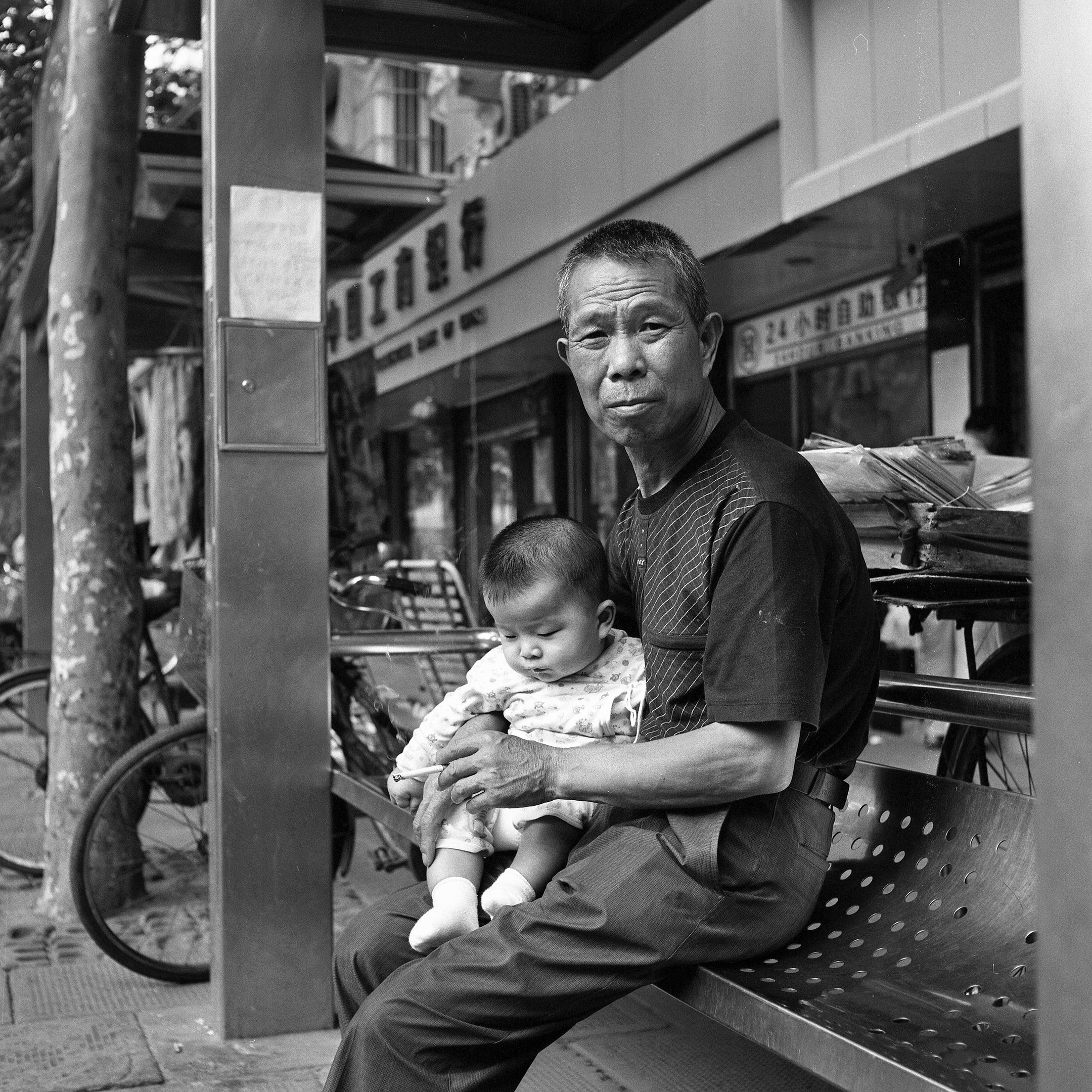 Man at bus stop holding grandchild and smoking a cigarette