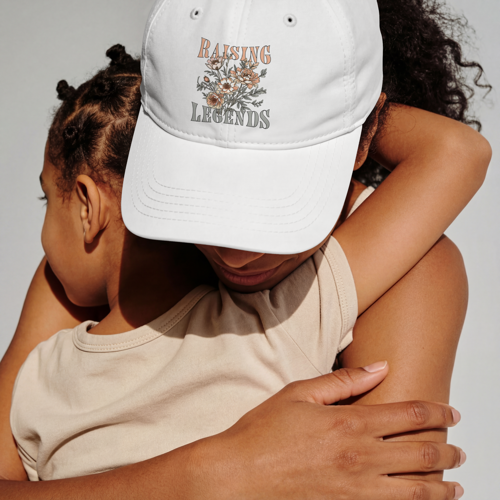 A mother wearing a white Raising Legends baseball hat designed by neurodivergent artist