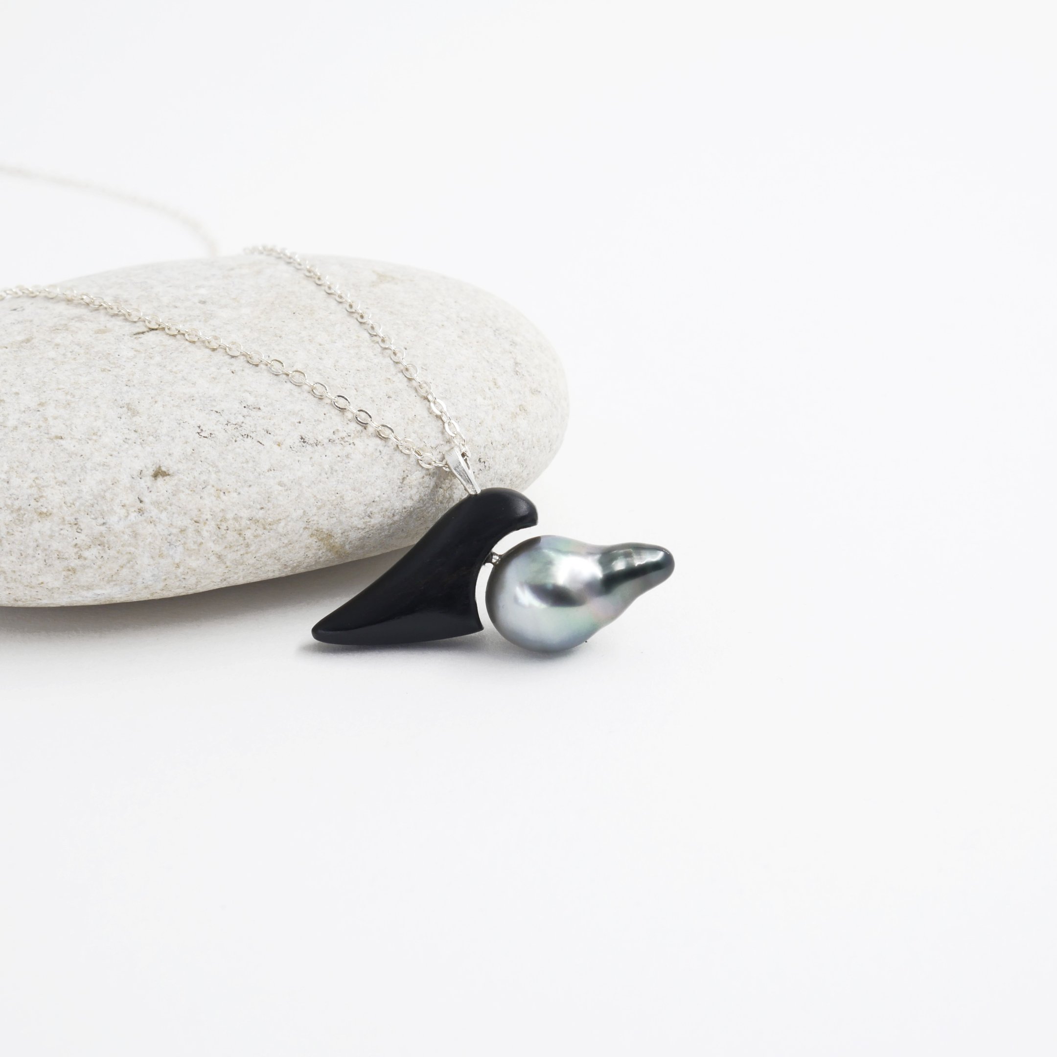 Handmade silver necklace featuring a black onyx gemstone and a grey baroque pearl on a white stone.