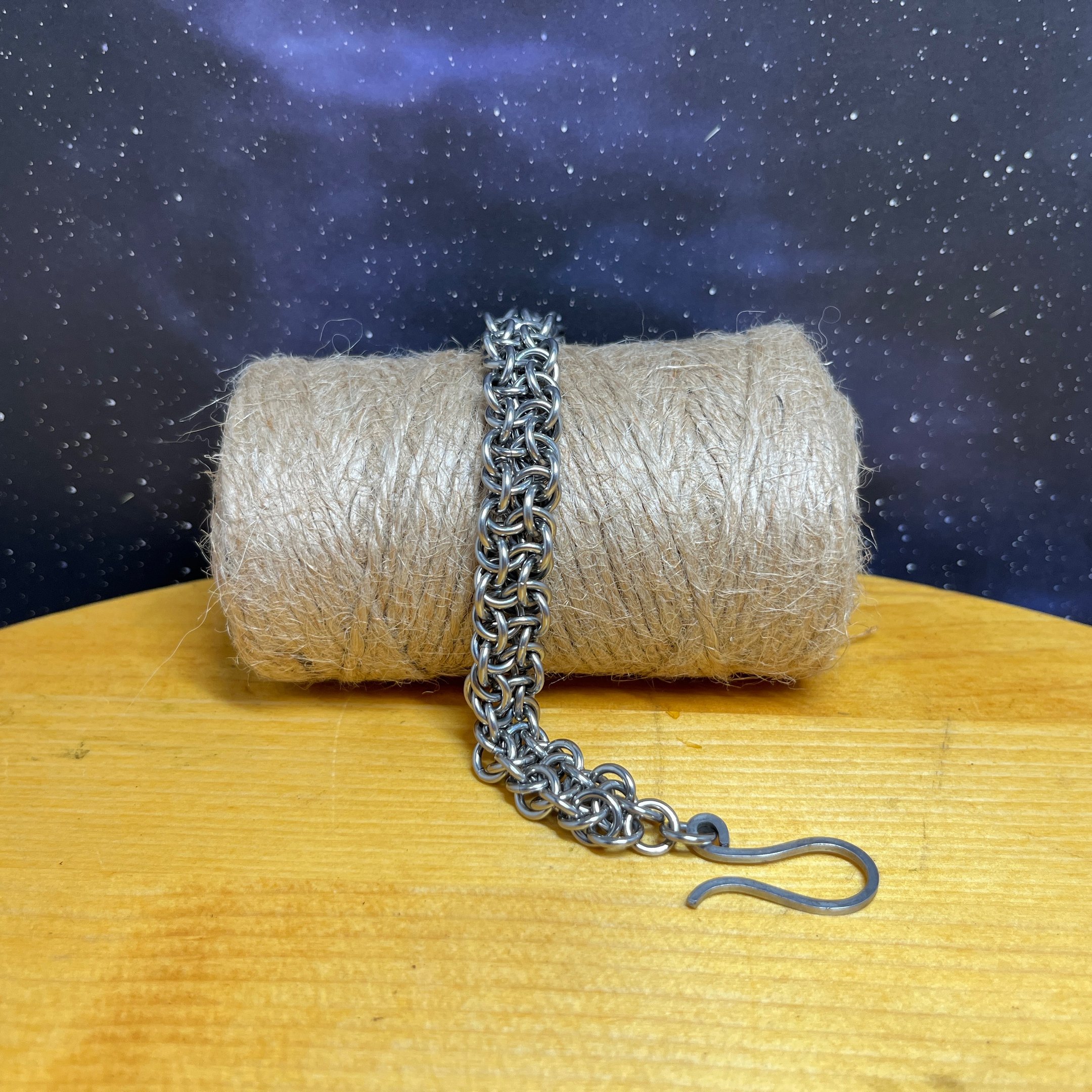 Photo of a chainmaille bracelet made of stainless steel draped over a bundle of jute twine