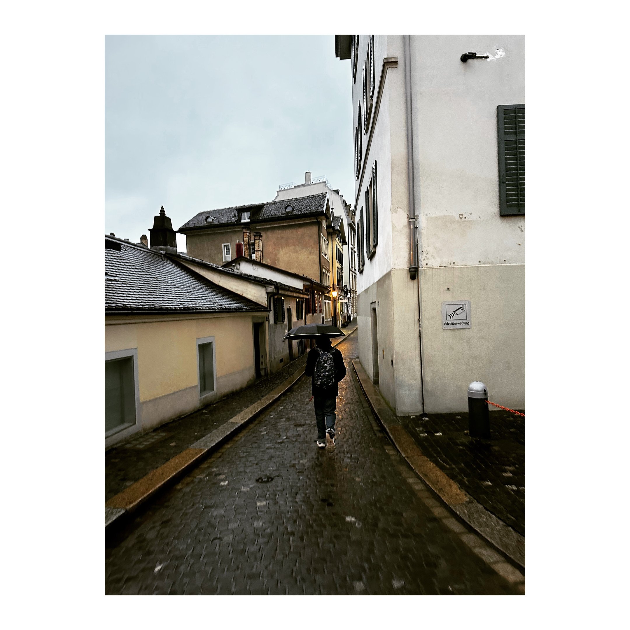 A person walks through narrow alleys holding their umbrella in rainy Switzerland photography by LV