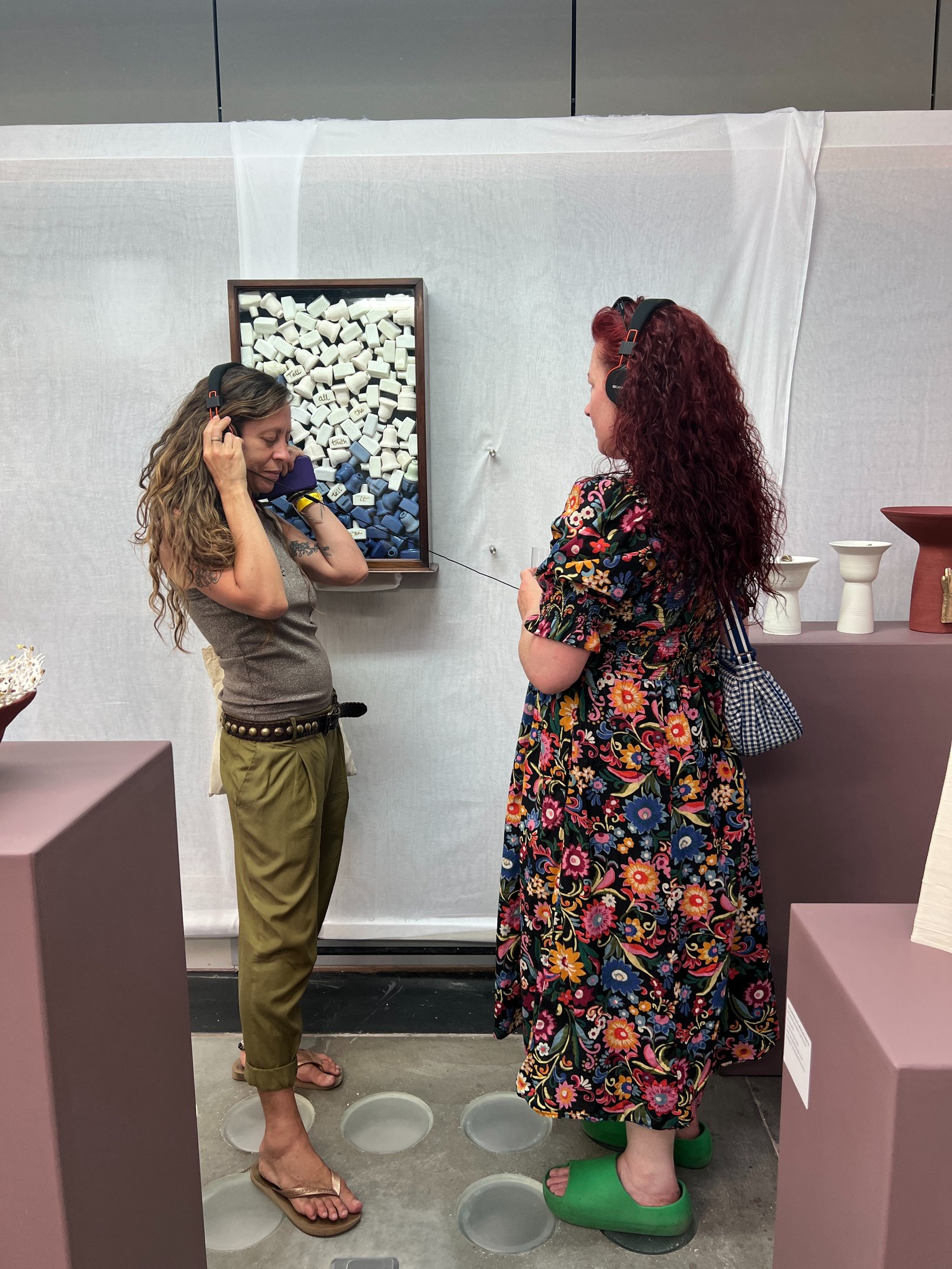 2 visitors listen to an audio installation, looking at a sculpture of Victorian ink bottles