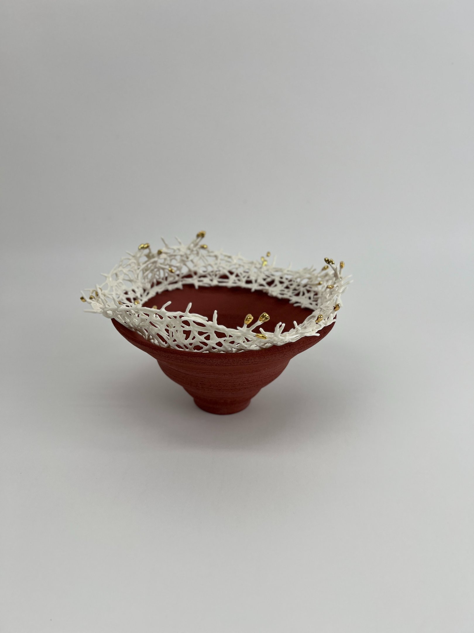 A thrown stoneware ceramic tiered bowl, topped with a porcelain white crown sculpture, tipped gold