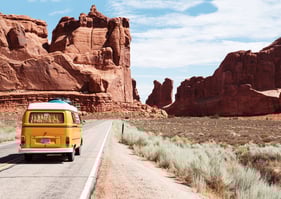 a yellow van driving down a road with moutain rocks in the background