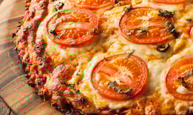 a vegan pizza with tomatoes and cheese on a wooden board